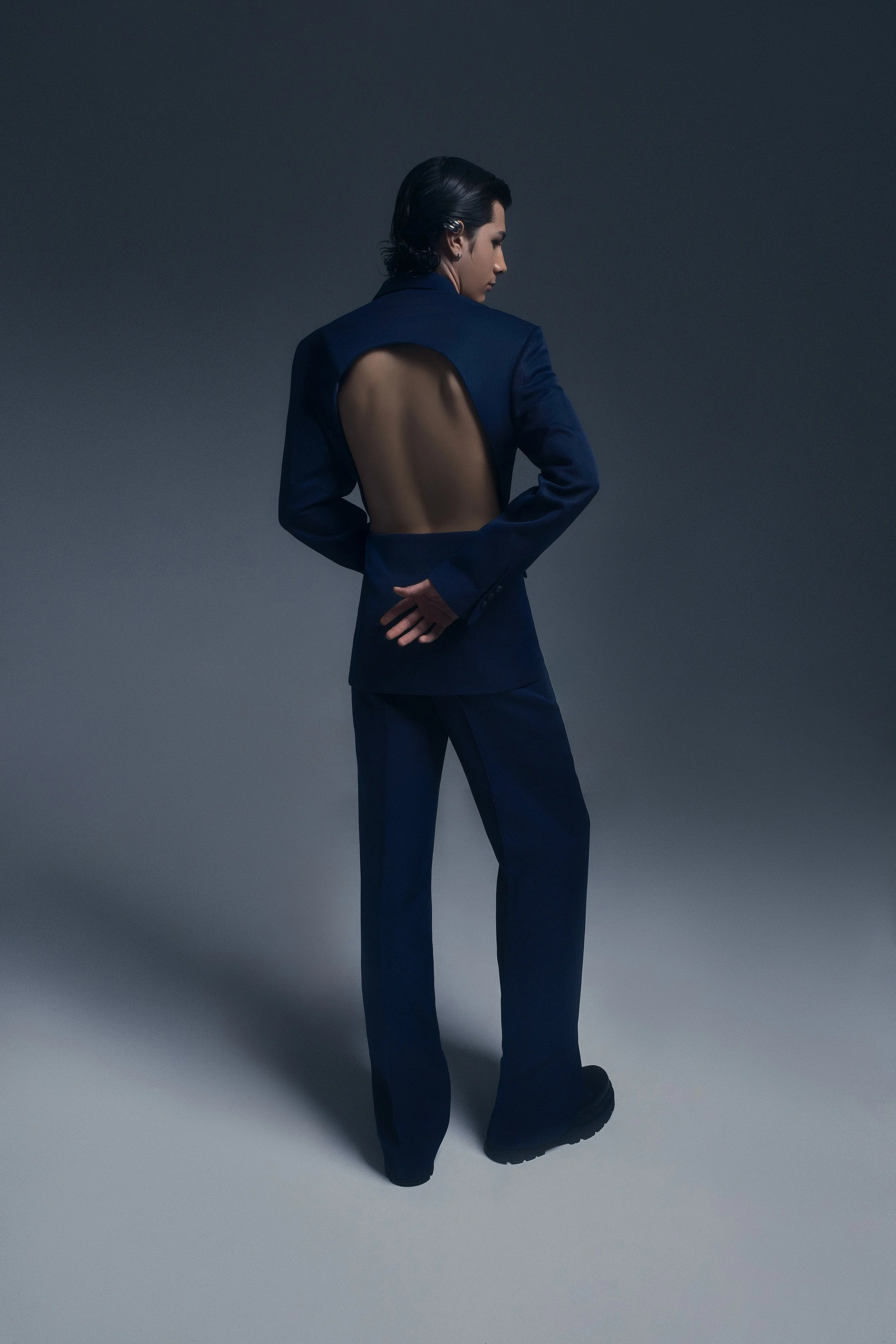 Persona con traje azul y espalda con corte de vestir, en un fondo gris oscuro.