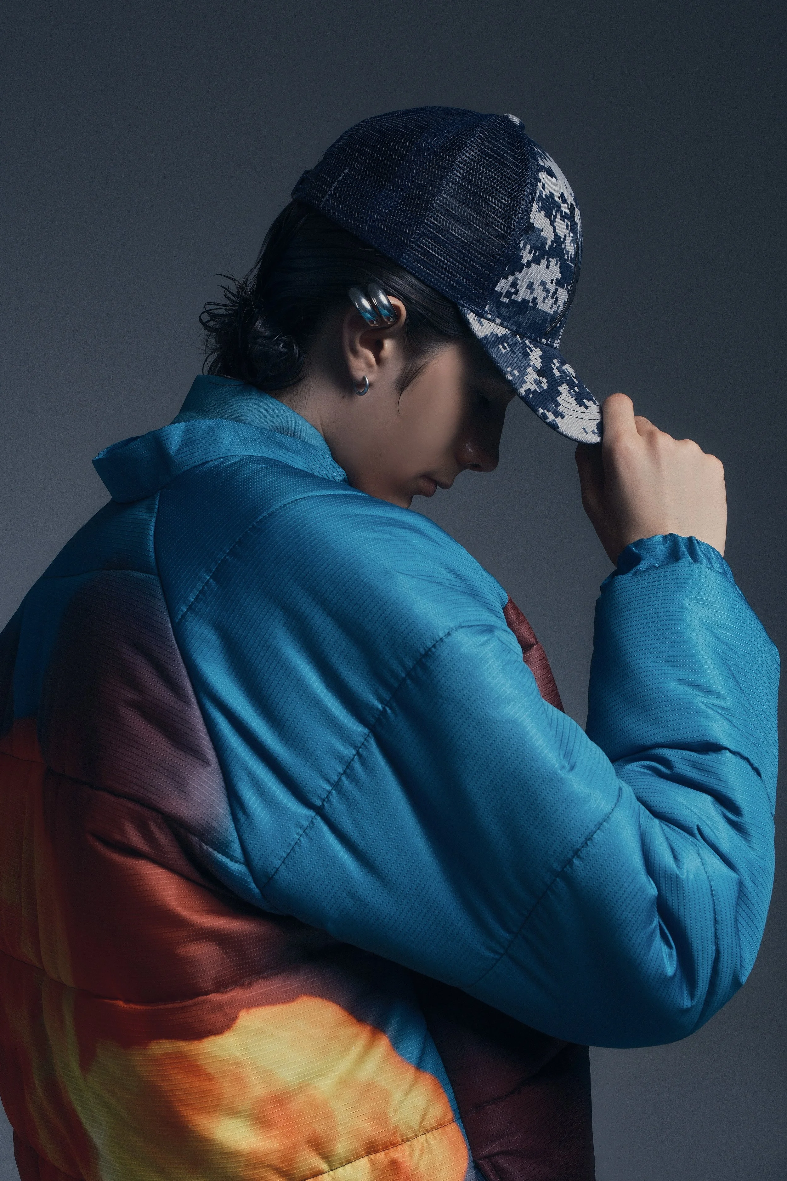 Persona con gorra de béisbol, chaqueta acolchada colorida, en postura pensativa.