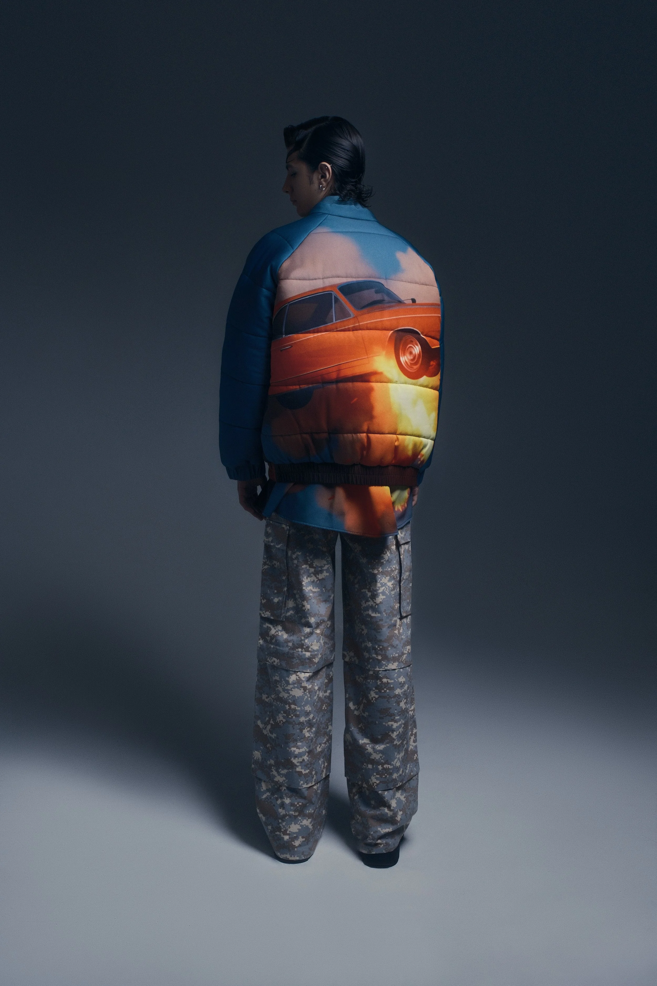 Persona vestida con chamarra con un diseño de coche y pantalones de camuflaje.