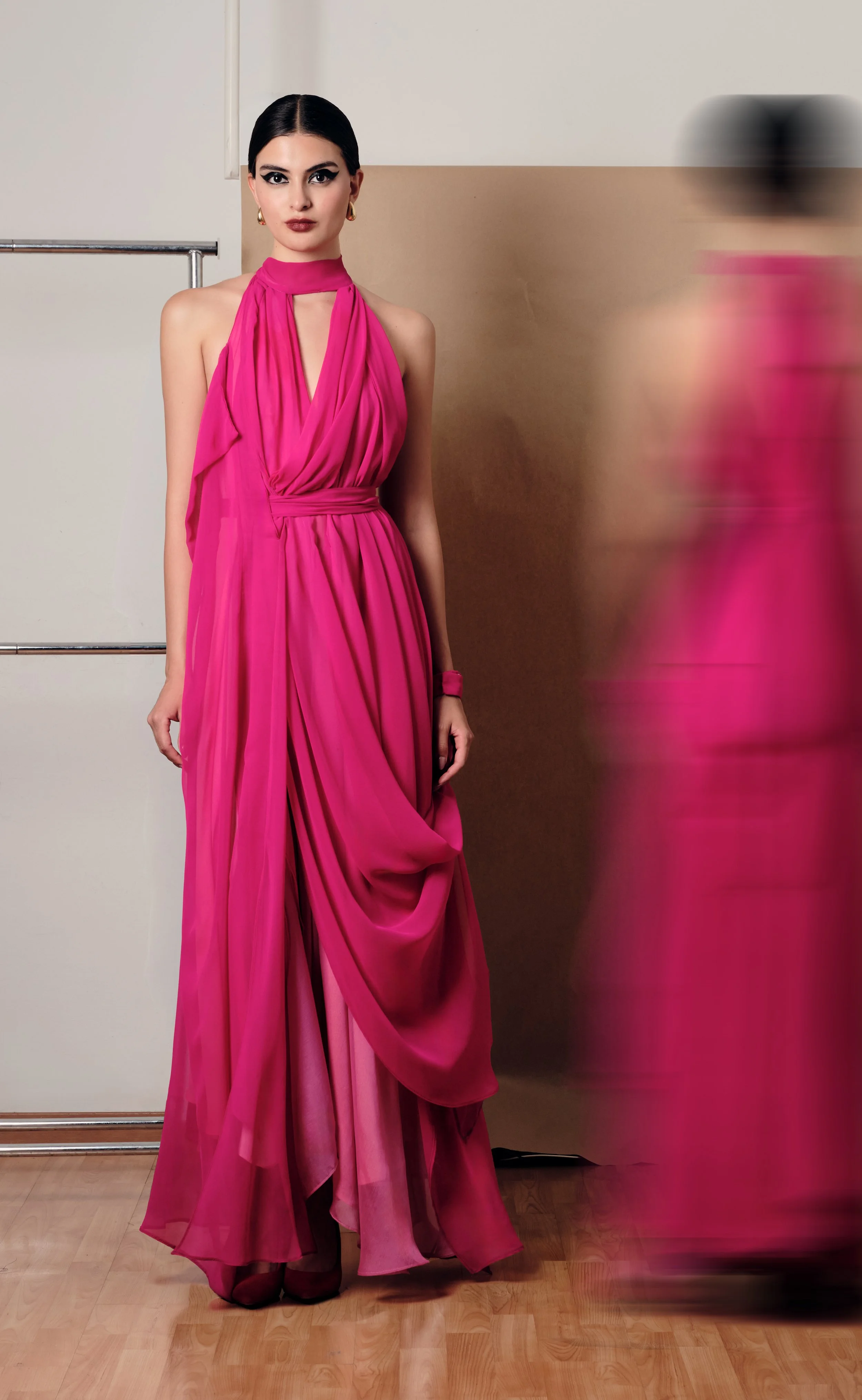 Mujer con vestido largo y rosa, con cabello oscuro y peinado liso, posando en un fondo neutral