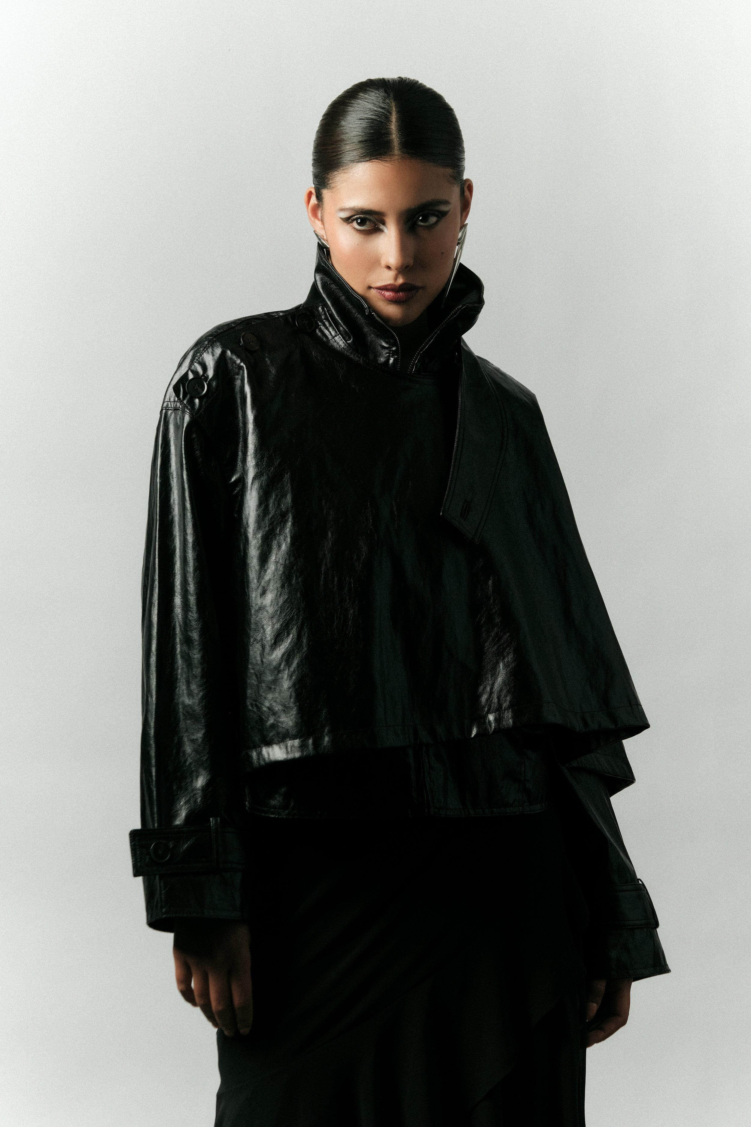 Mujer con cabello oscuro, peinada en chongo, viste una chaqueta de cuero negra y lleva un atuendo negro.