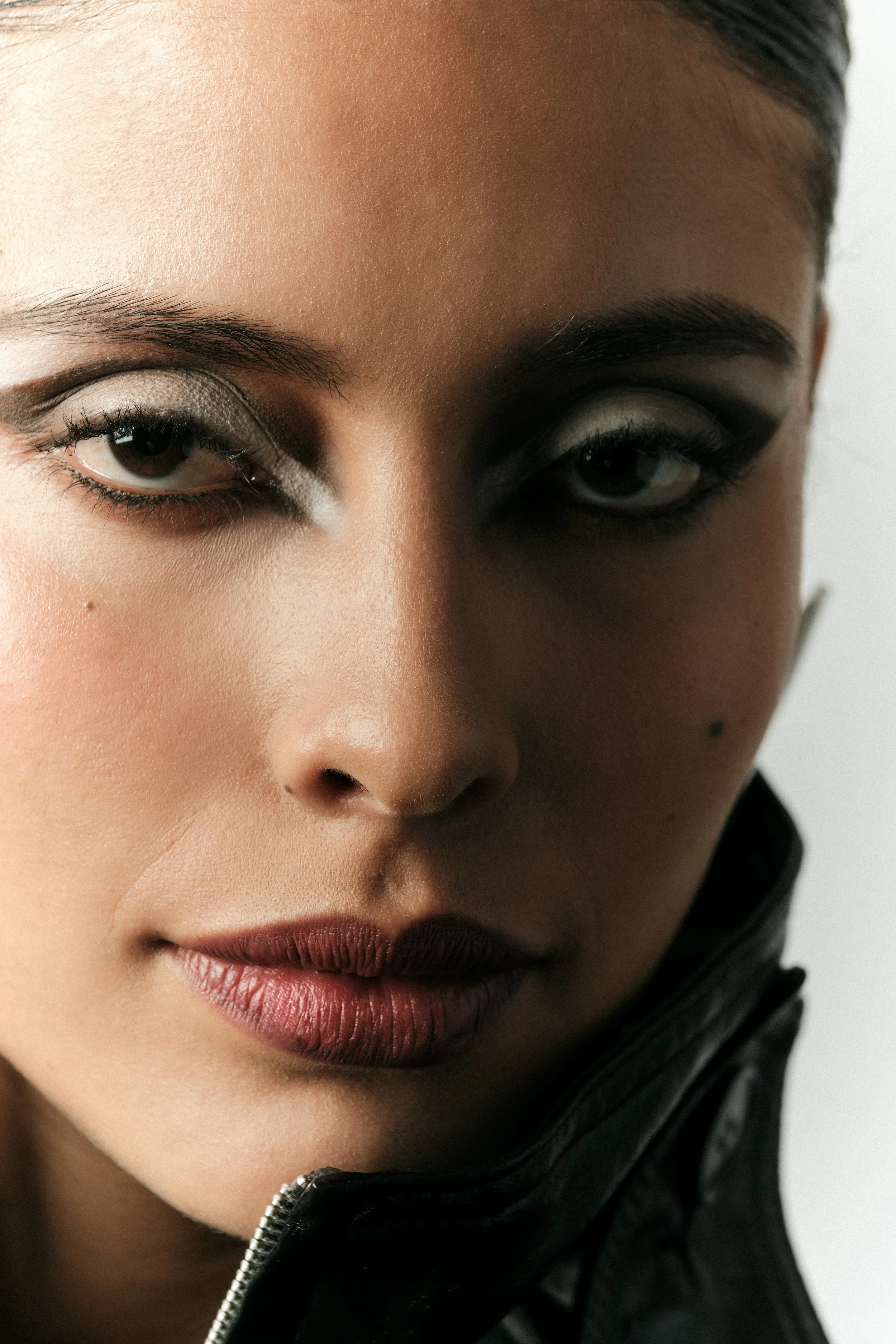 Retrato cercano de una mujer de piel clara con maquillaje llamativo, labios oscuros y ropa negra