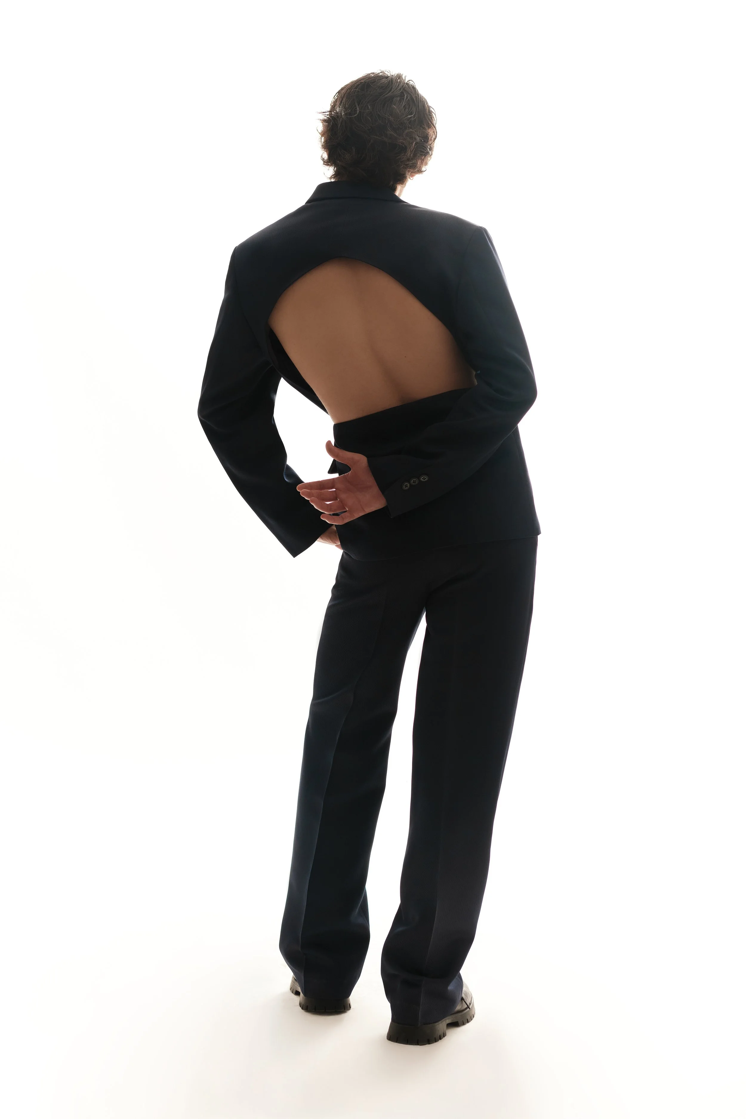 Persona con traje negro que muestra una espalda descubierta, de espaldas, en un fondo blanco.