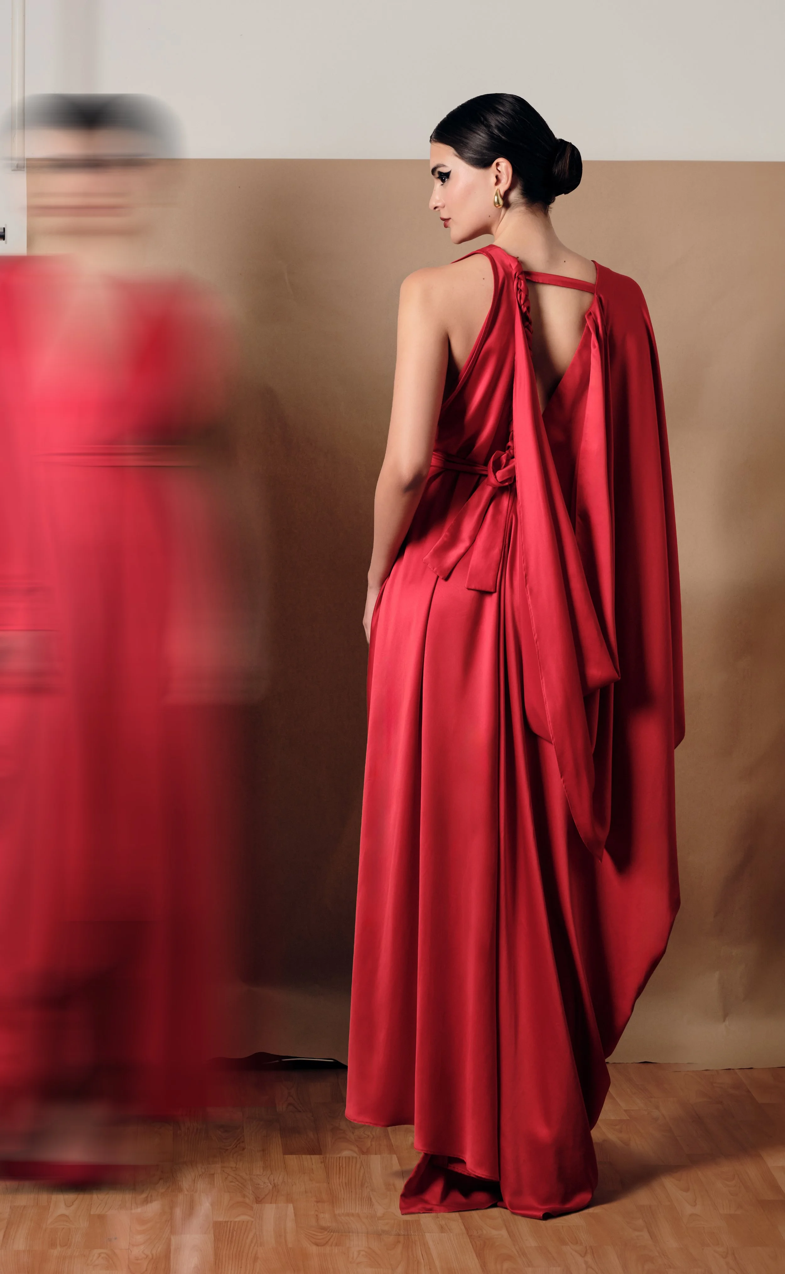 Mujer con vestido largo y rojo, observando de perfil en un fondo neutral.