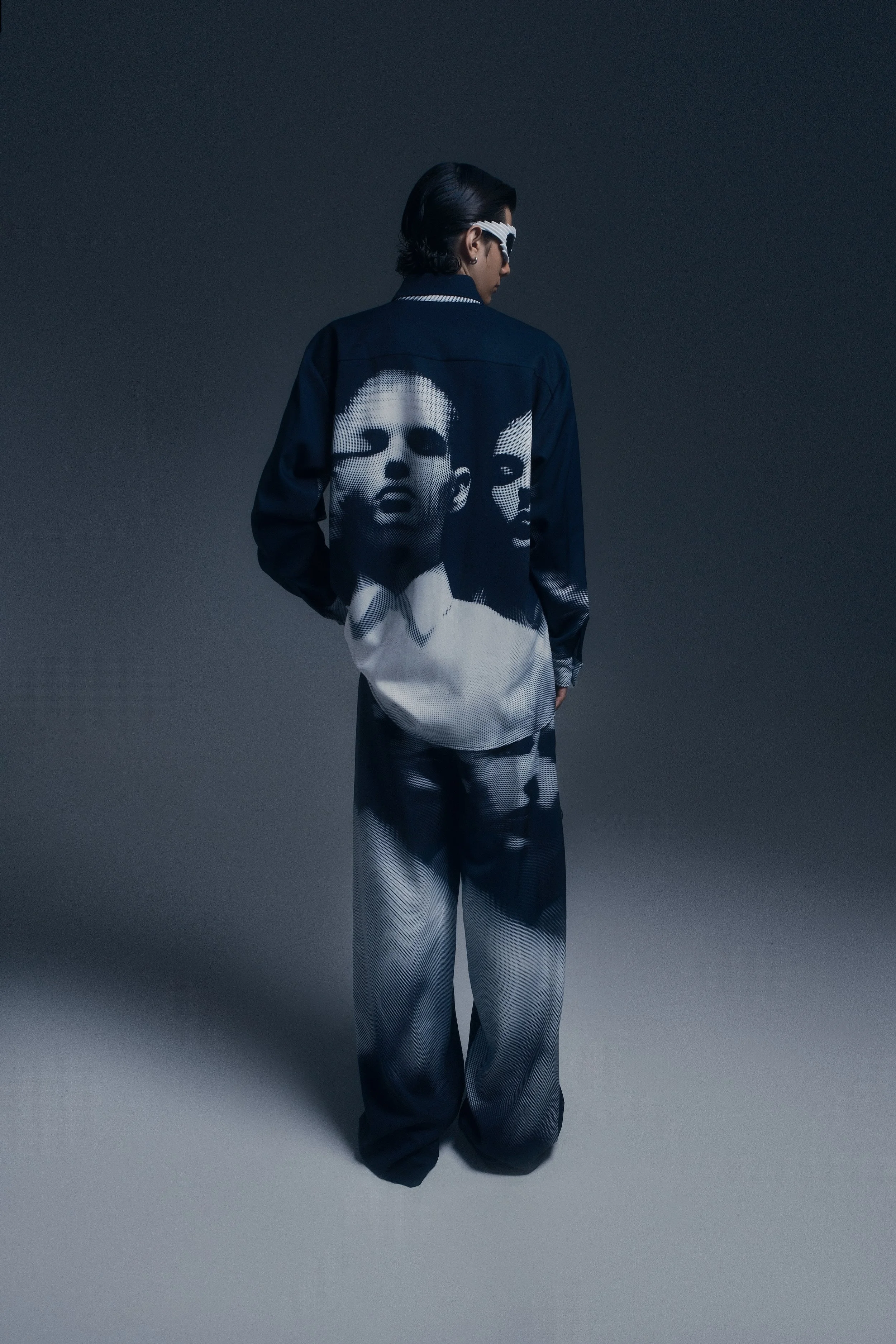 Persona con vestido y pantalones decorados con imágenes en tonos oscuros de rostros humanos en estilo artístico.