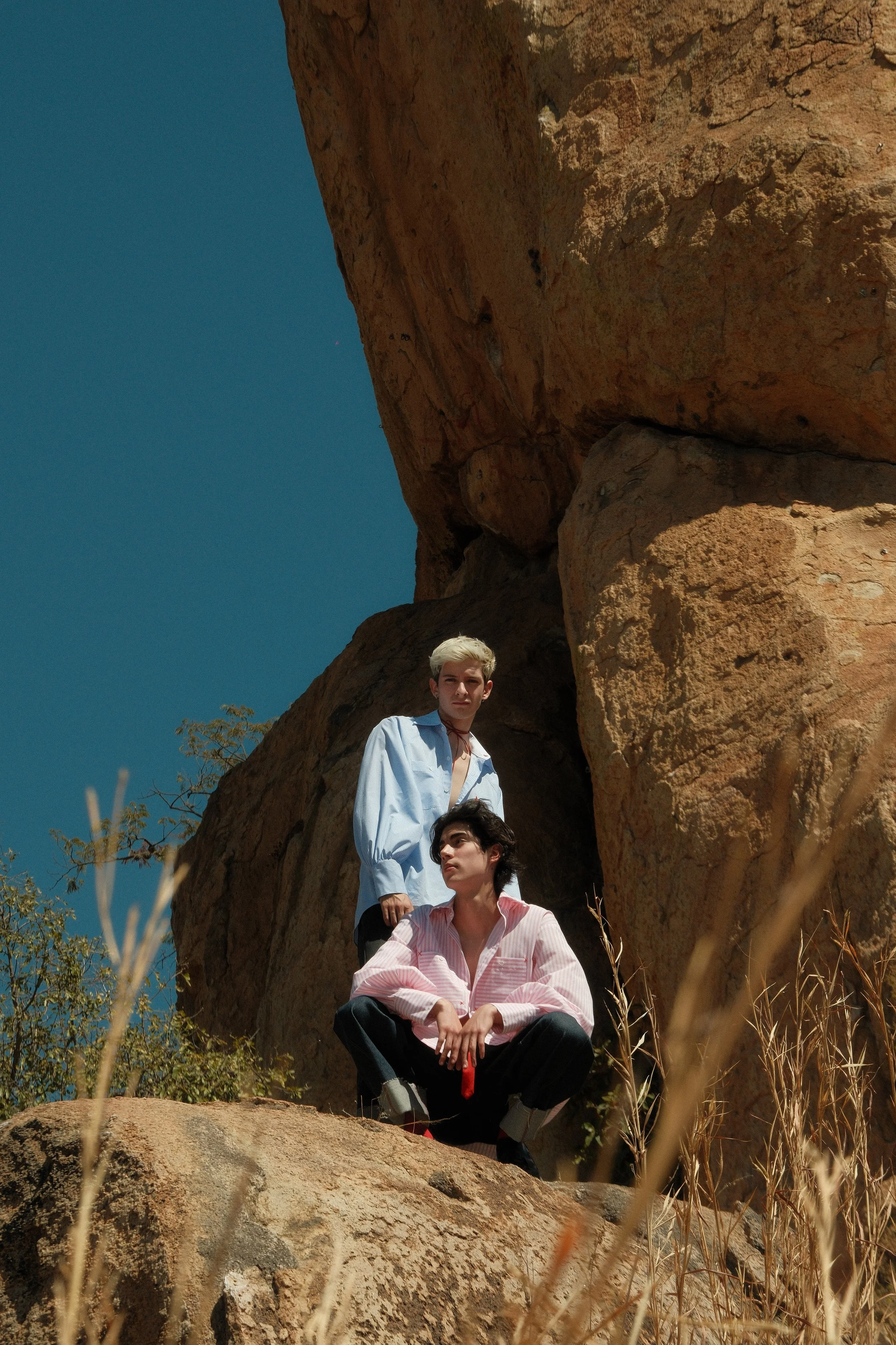 Dos jóvenes posando en un entorno rocoso y soleado con cielo despejado.