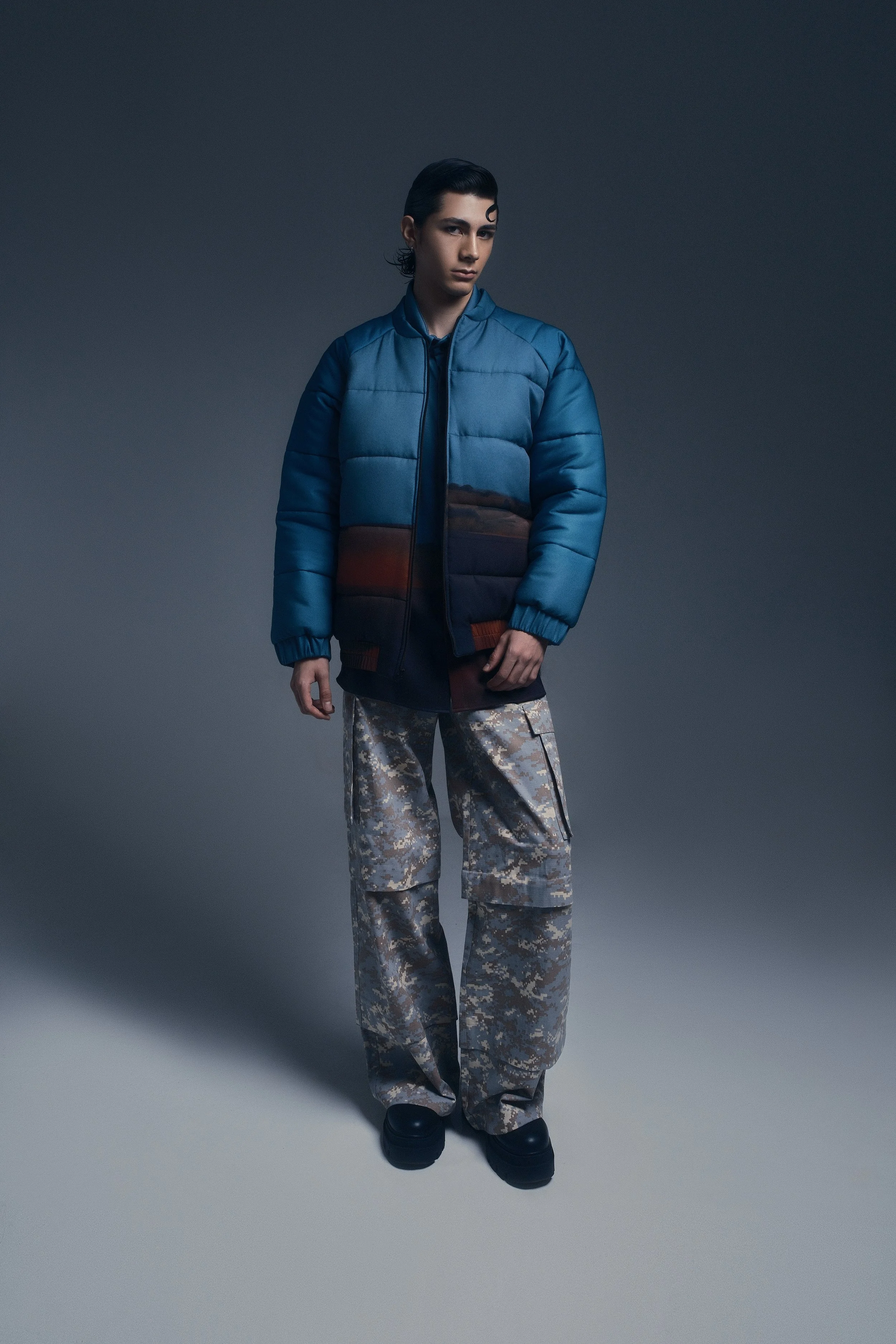 Persona con chaqueta azul y pantalones de camuflaje en un fondo gris