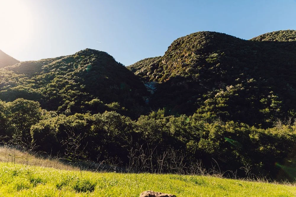 Scenic view of green hills under clear blue sky with sunlight.