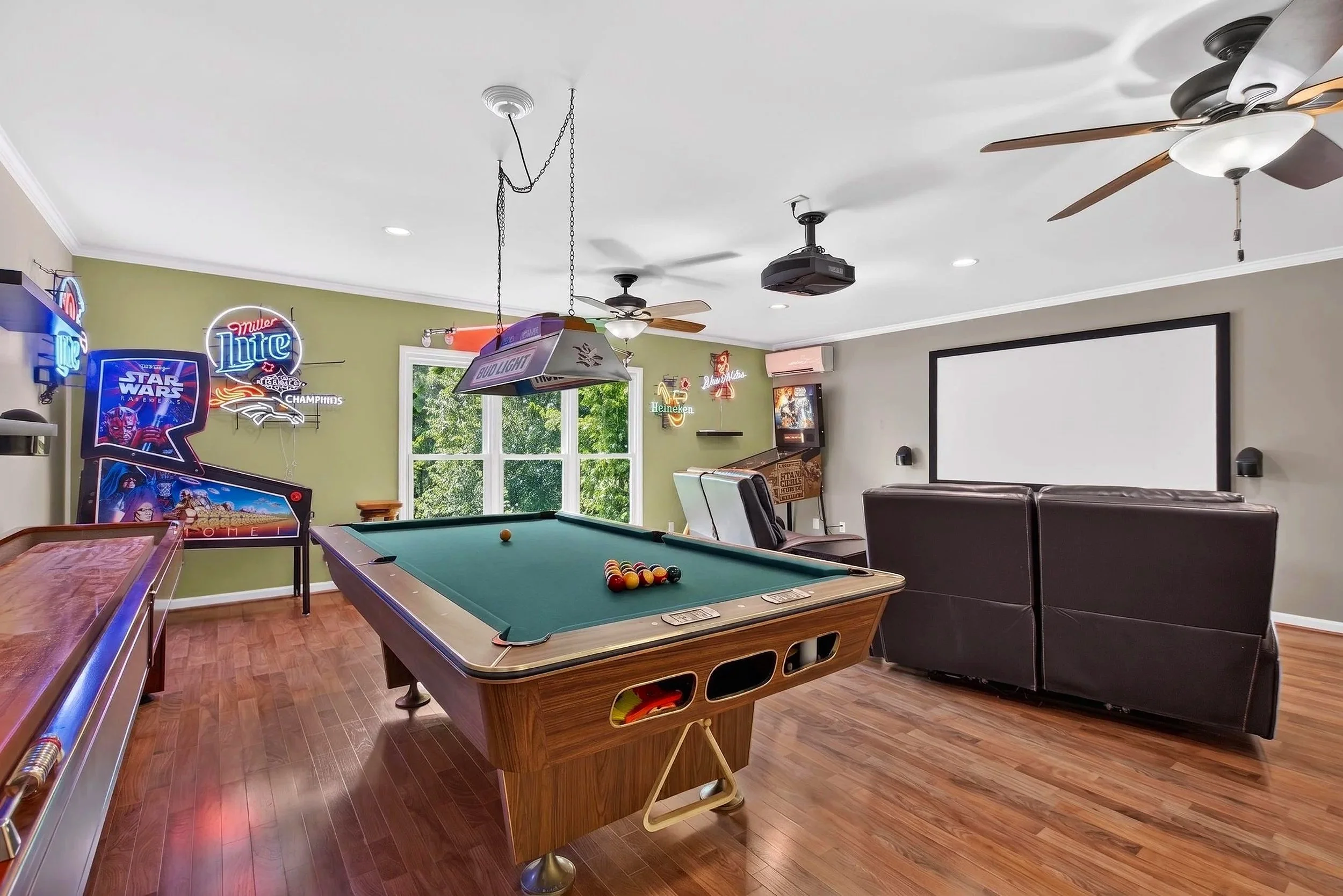 A game room with a pool table, neon signs, arcade game, and a large wall projection screen.