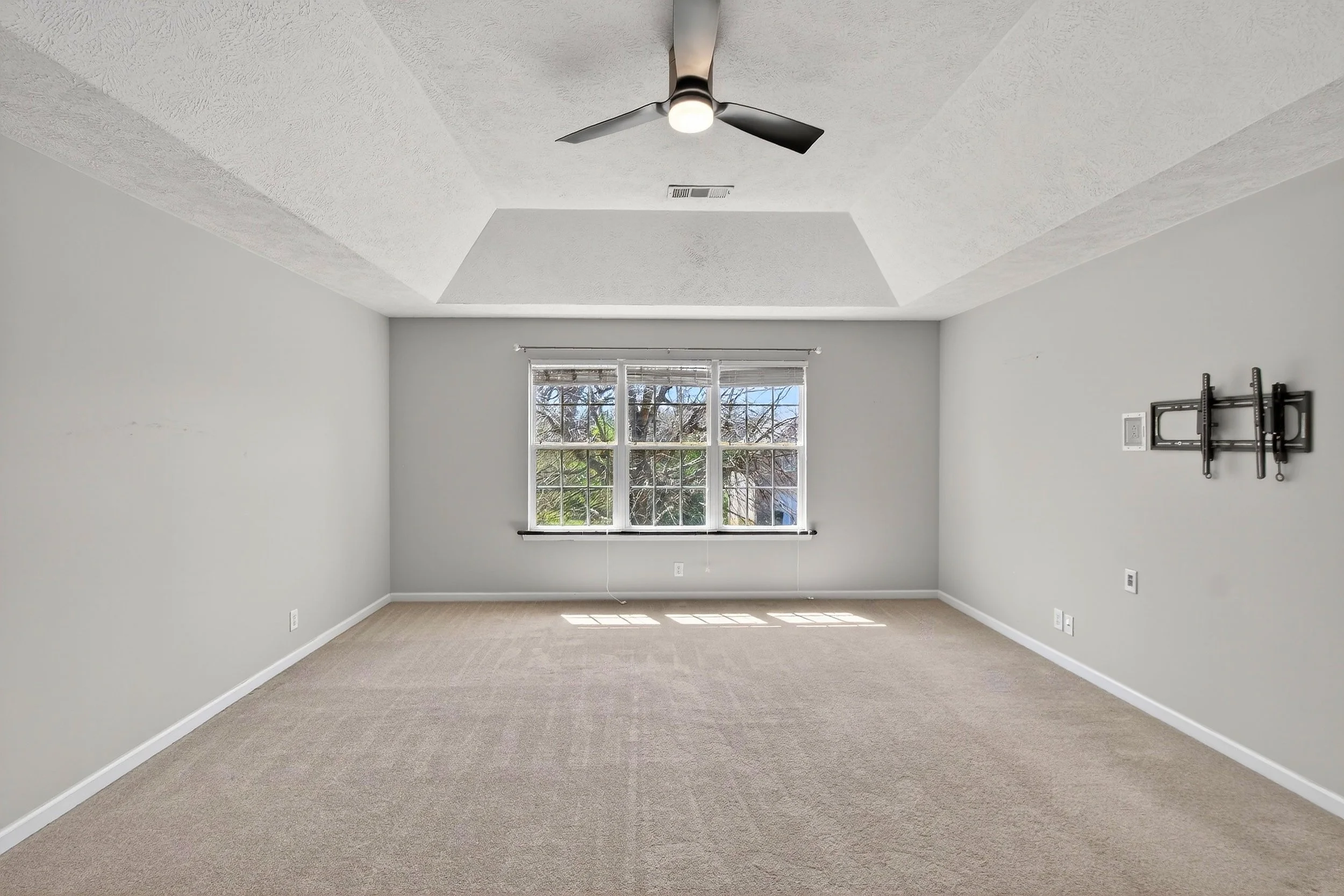 Empty room with a large window, ceiling fan, beige carpet, and white walls.