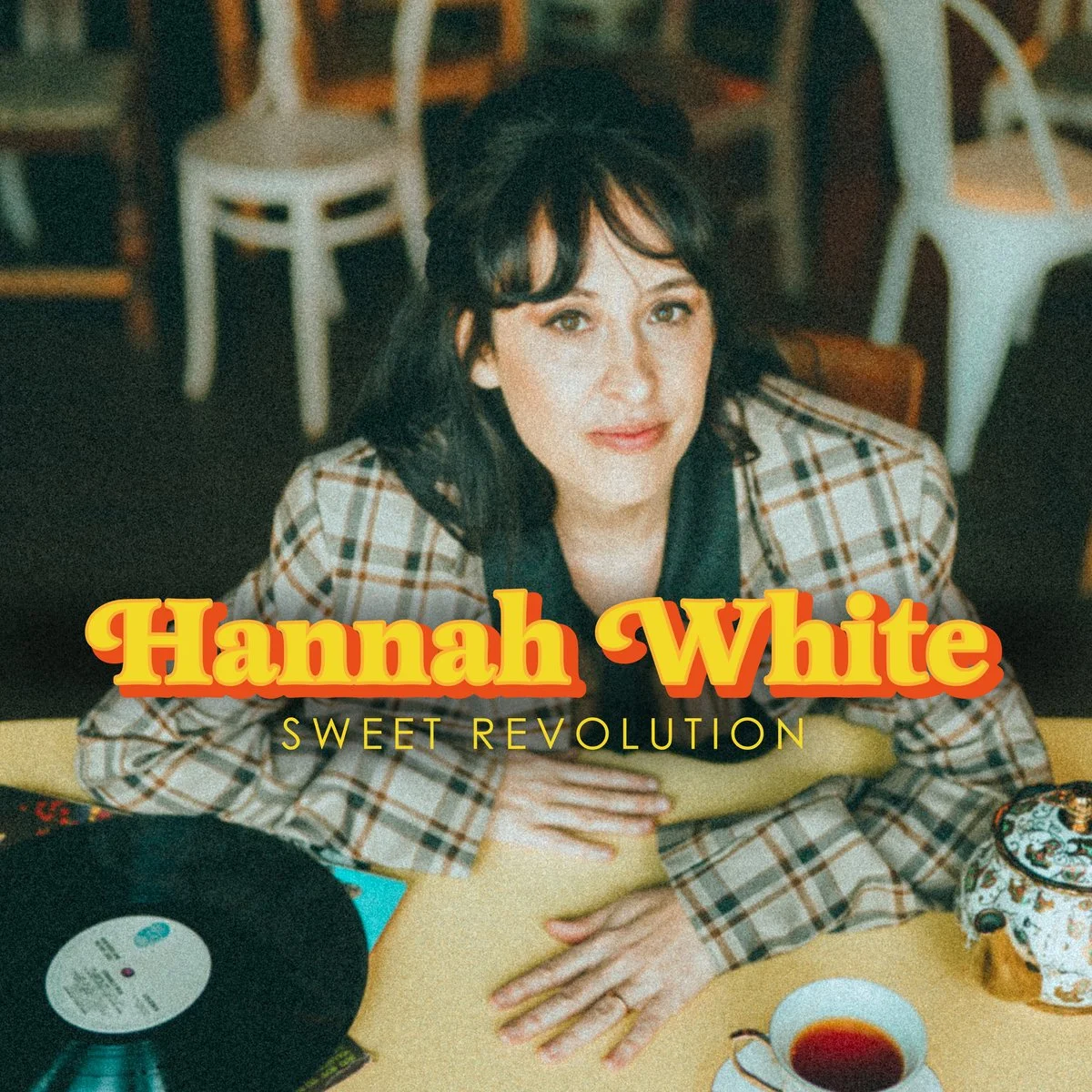 Cover image of a woman with dark hair and a plaid blazer sitting at a table with a vinyl record, a cup of tea, and a teapot, with the text "Hannah White" and "Sweet Revolution" overlaid.
