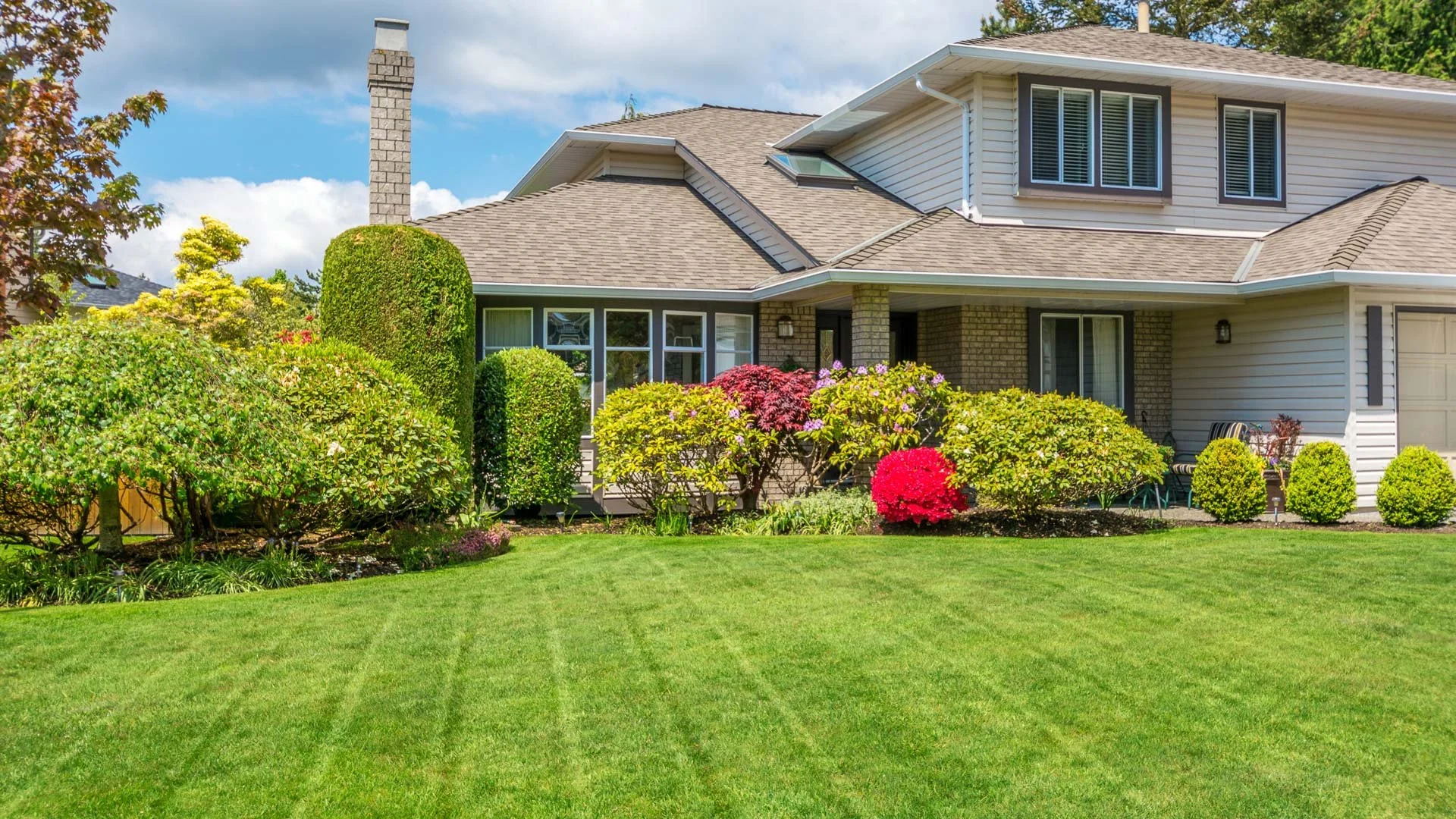 Front view of a suburban house with a well-maintained lawn and colorful garden plants.