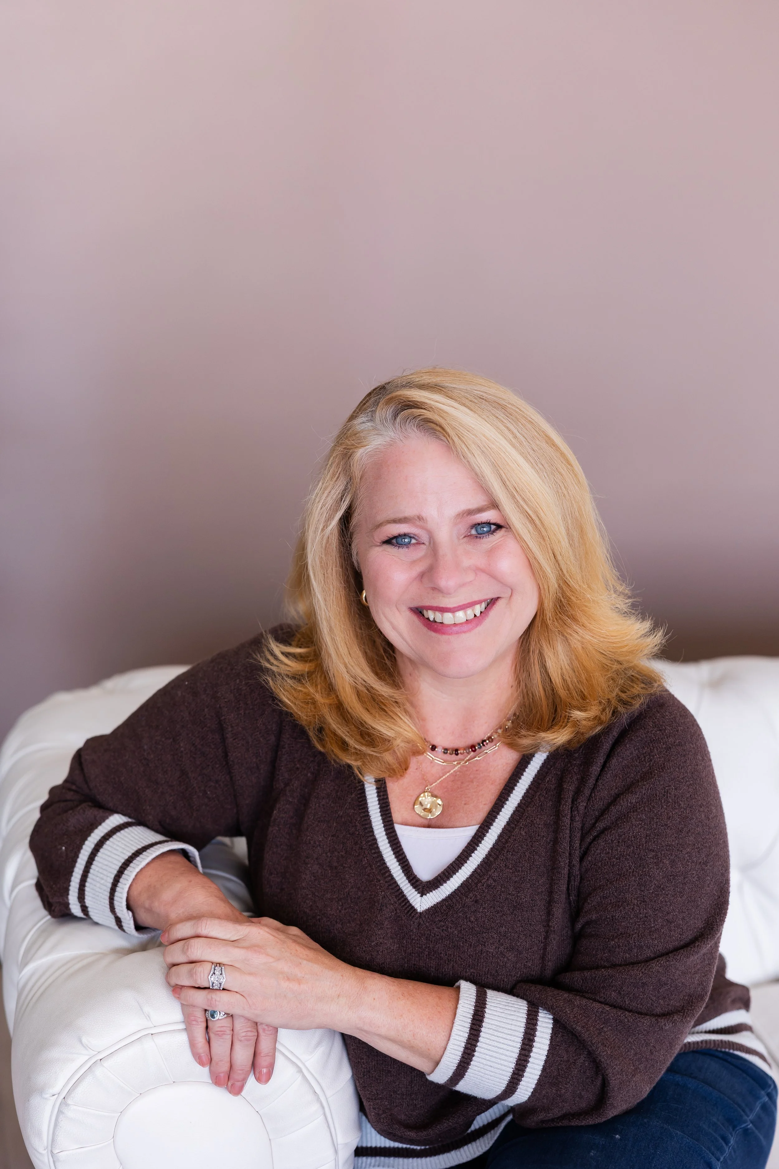 Life coach Lisa Summers, wearing a brown sweater and sitting on a white sofa.