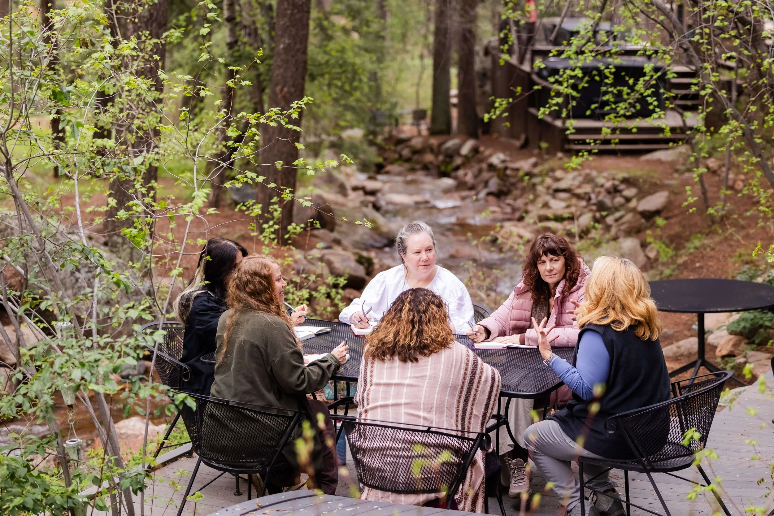 A group of women sitting around a black metal outdoor table at a mountain coaching retreat.