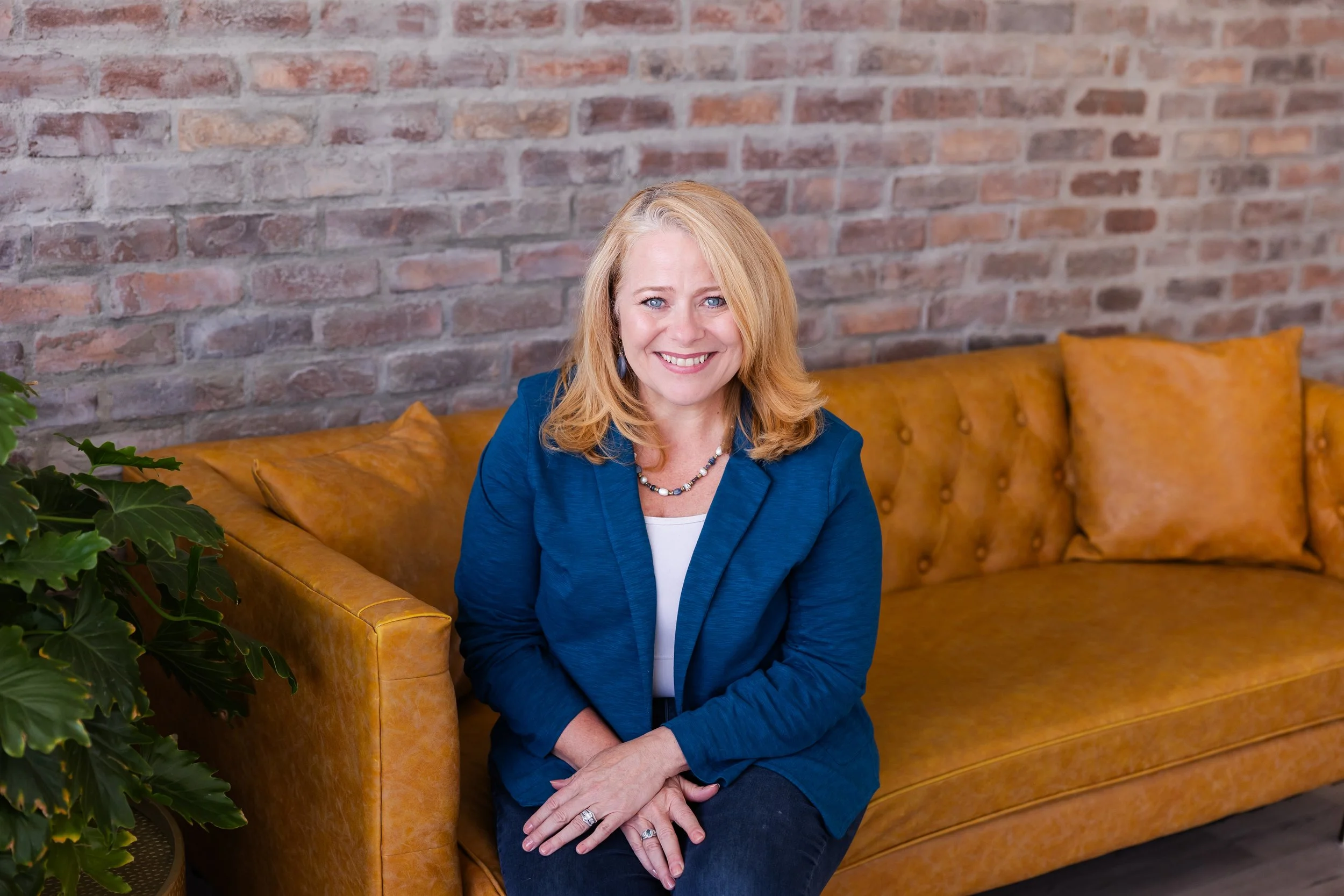 Lisa Summers, life coach, with blonde hair, blue eyes, smiling and sitting on a mustard-colored sofa