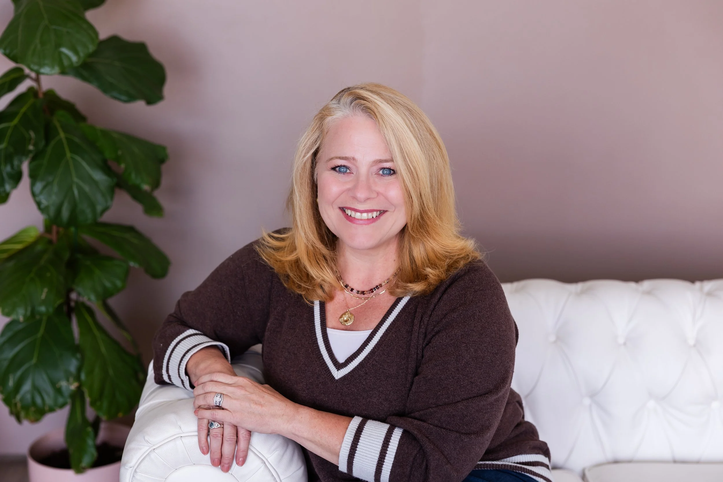 Life coach Lisa Summers, wearing a brown sweater and sitting on a white sofa.