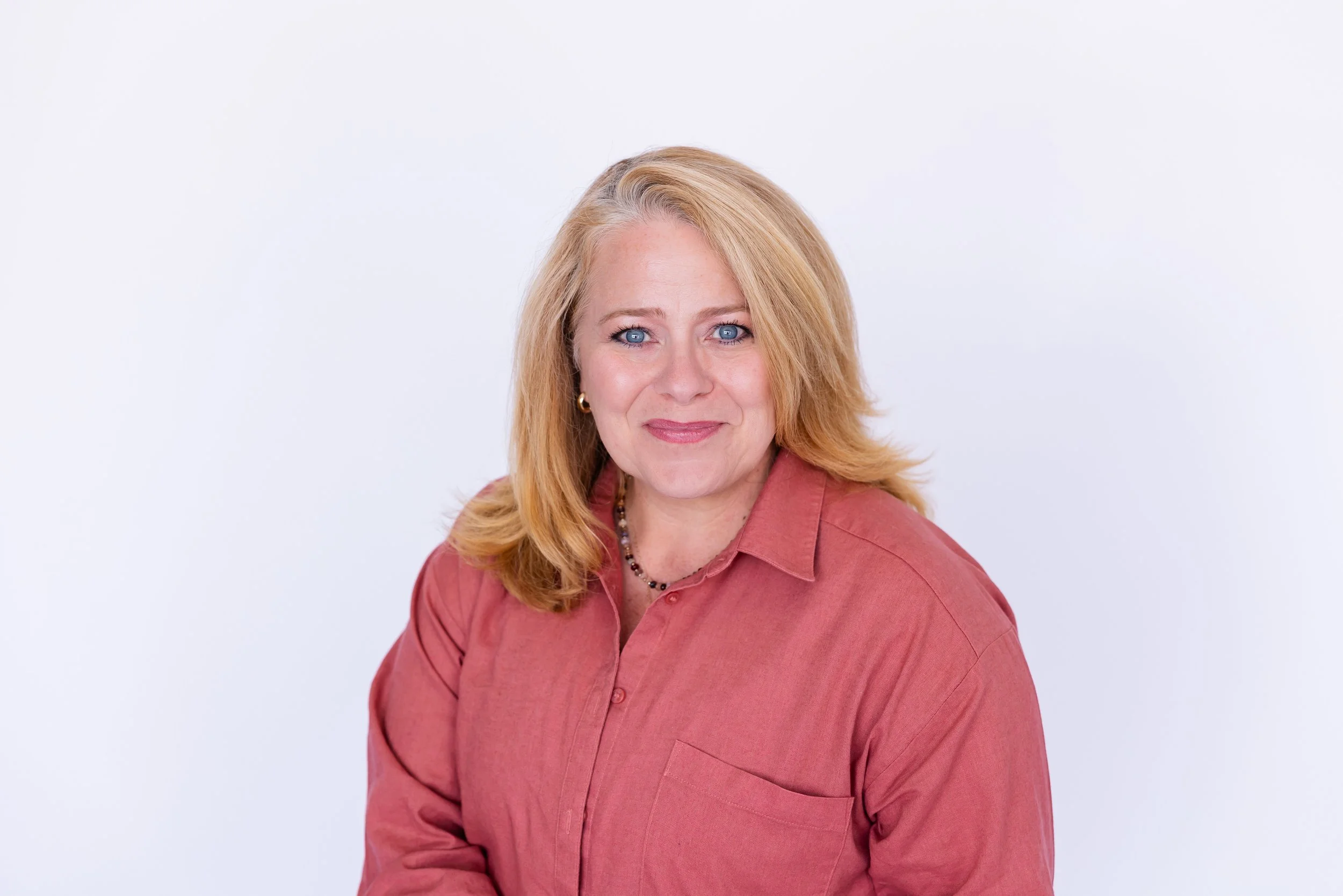 Lisa Summers, life coach, with blonde hair, blue eyes, wearing a pinkish-coral shirt, smiling, against a plain white background.