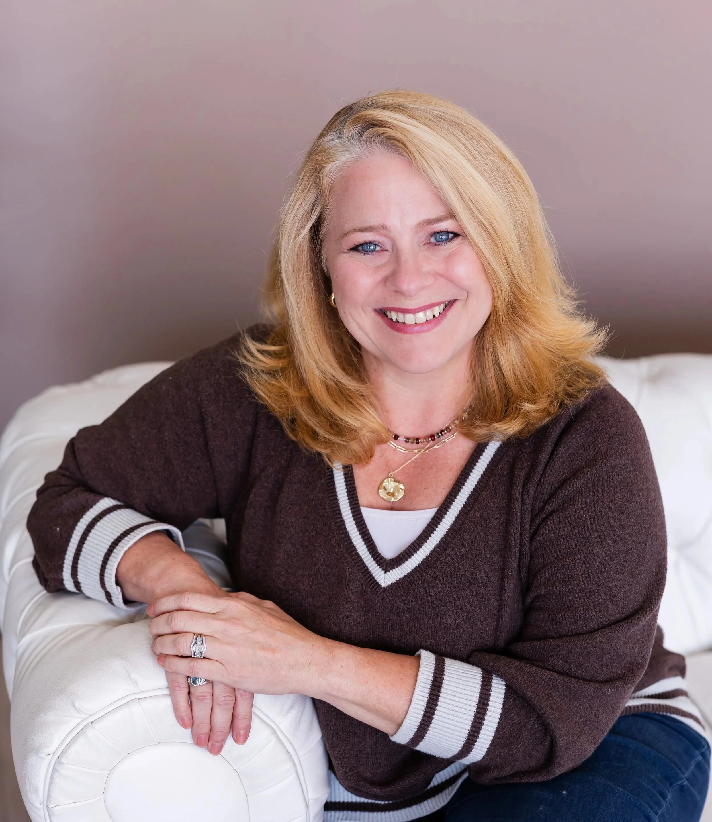 Life coach Lisa Summers, wearing a brown sweater and sitting on a white sofa.
