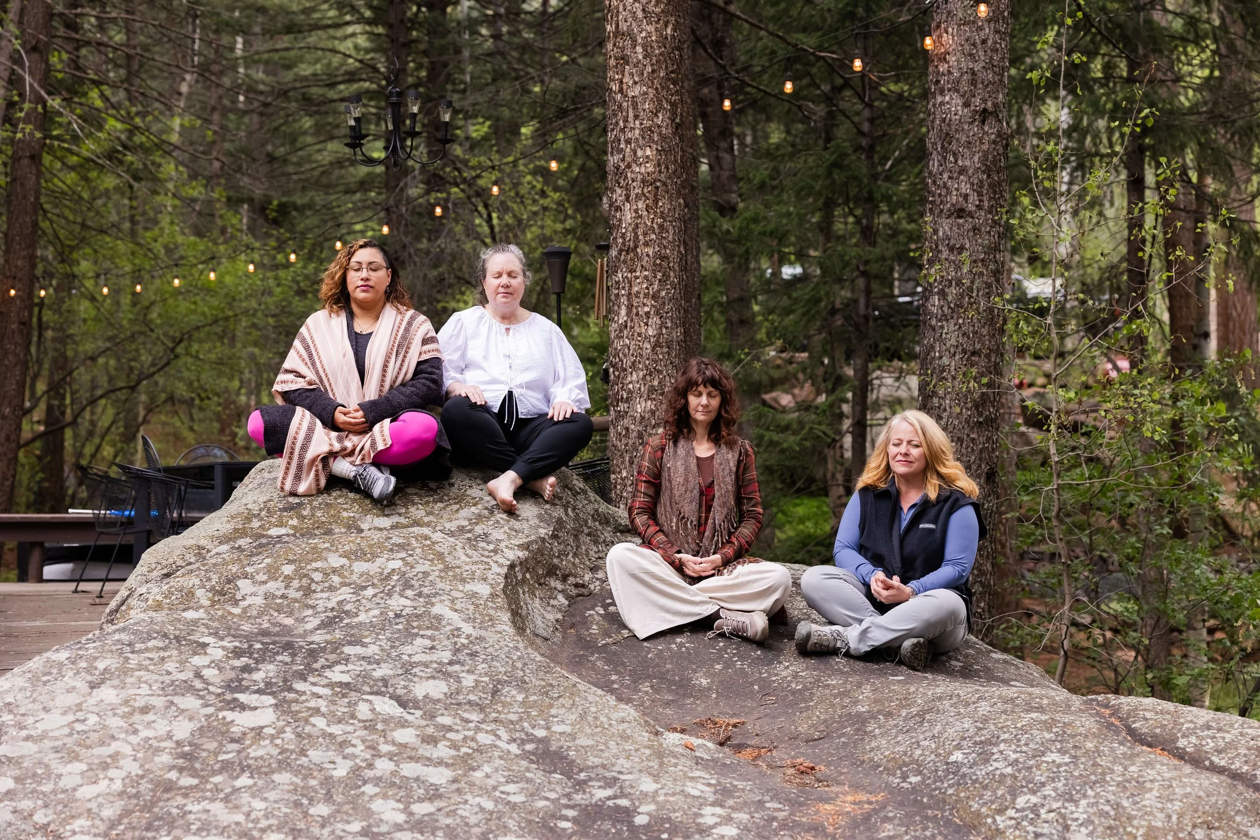Four women meditating outdoors on rocks in a Colorado mountain retreat