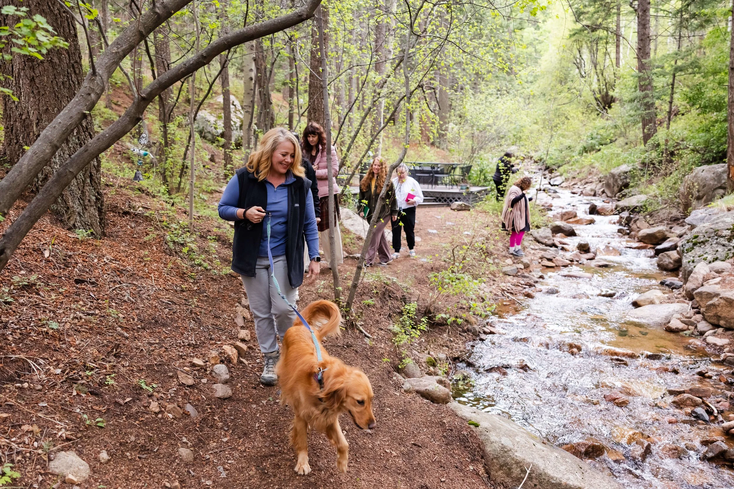 A women's wellness retreat in the Colorado mountains, walking along a forest trail beside a creek.