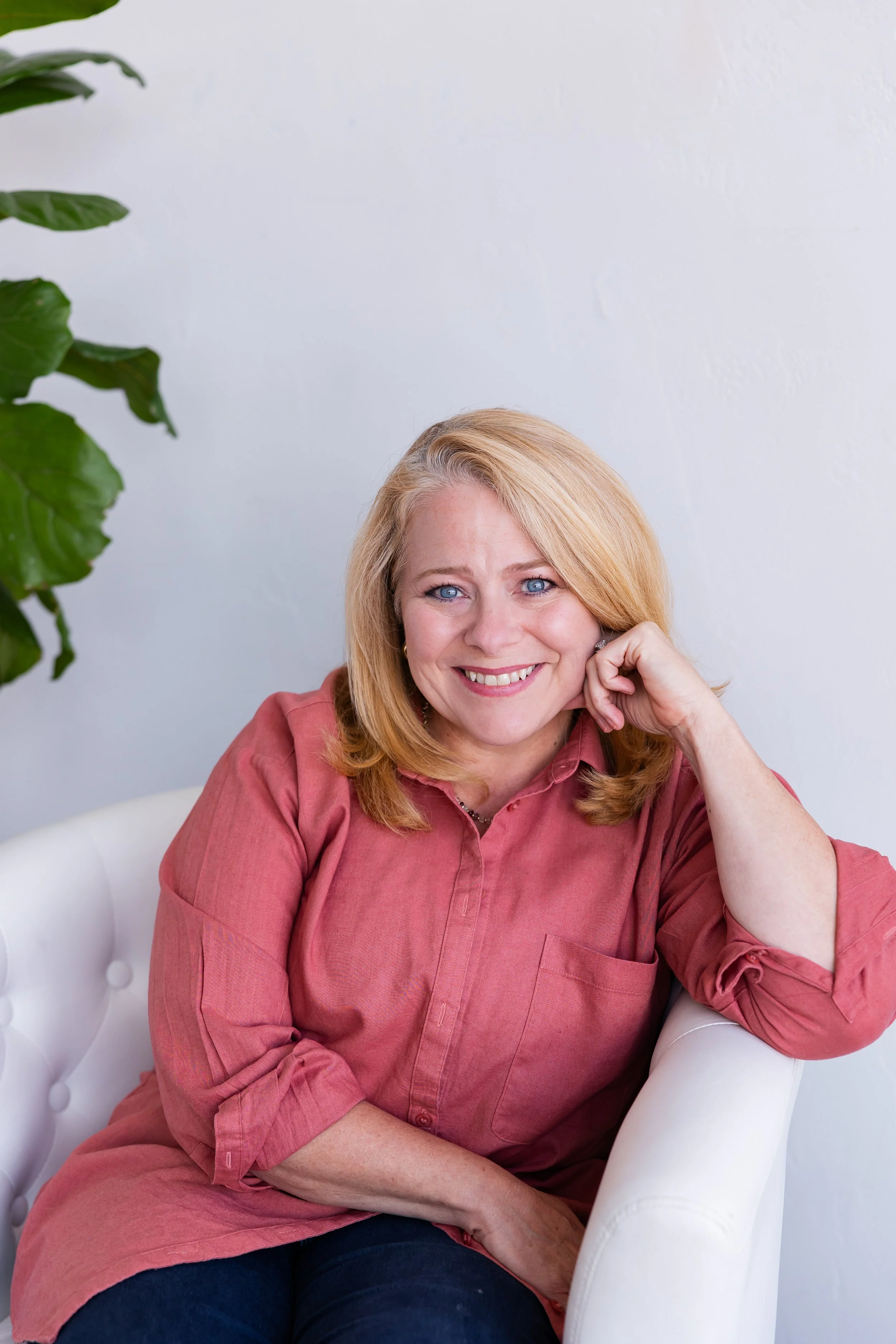 Lisa Summers, life coach, with blonde hair, blue eyes, wearing a pinkish-coral shirt, smiling, against a plain white background.