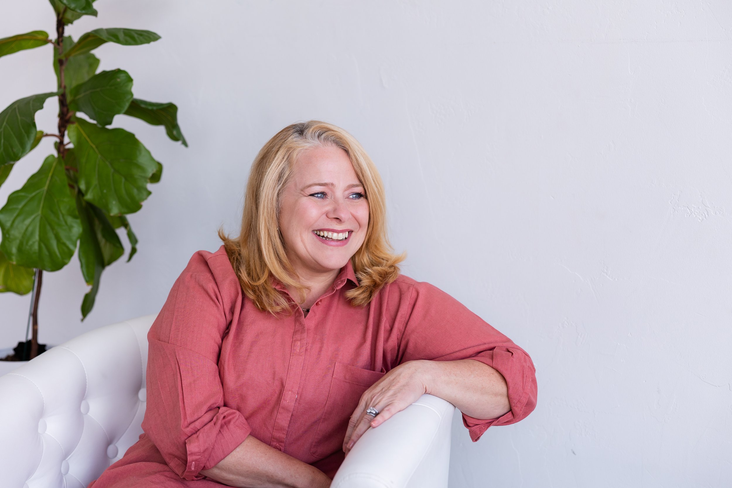 Lisa Summers, life coach, with blonde hair, blue eyes, wearing a pinkish-coral shirt, smiling, against a plain white background.