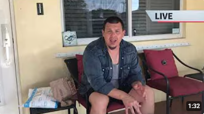 A man sitting outside on a porch, talking to the camera, with a