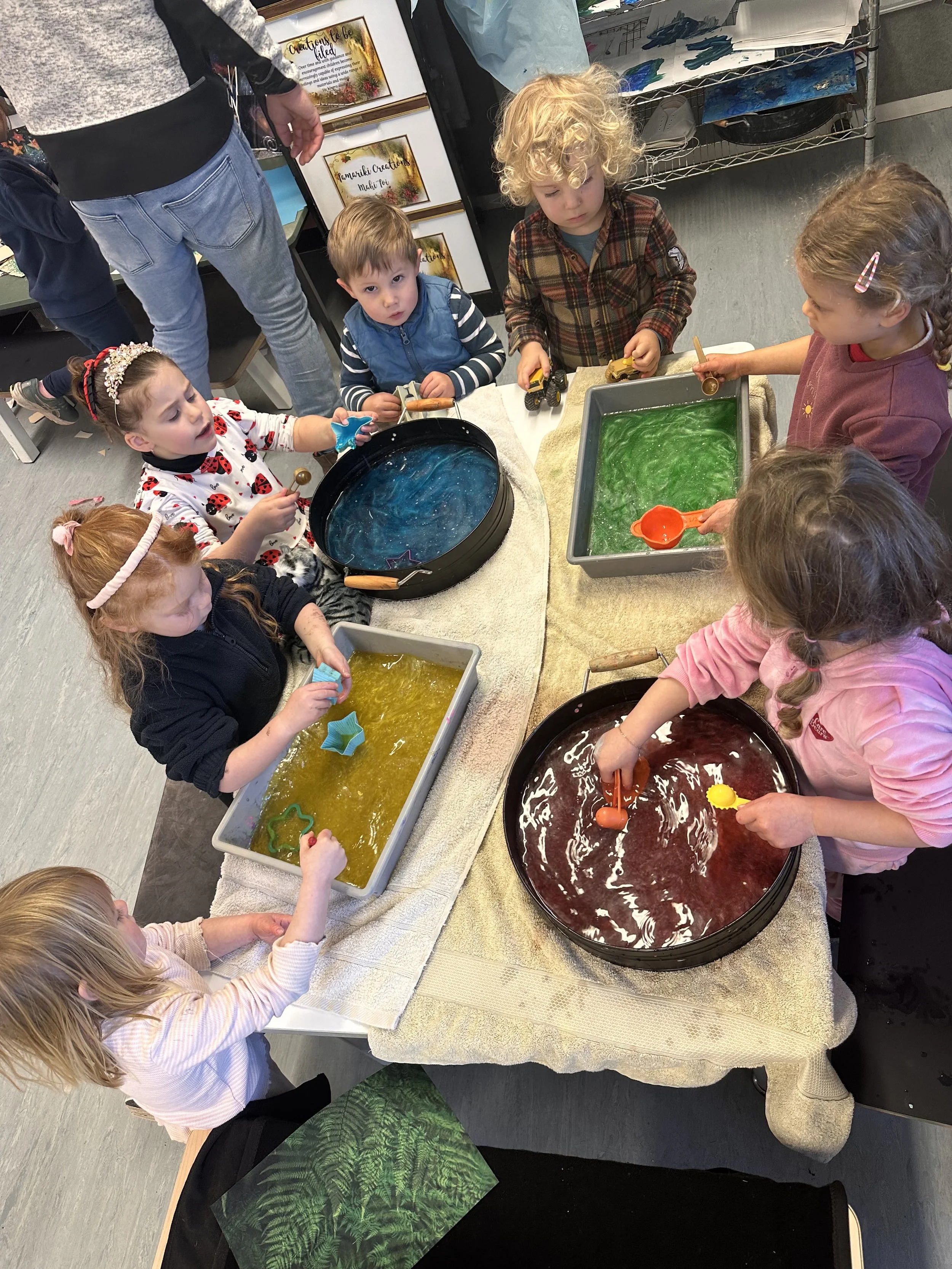 Children are engaging in a sensory activity with colorful slime and water play at a table, supervised indoors.