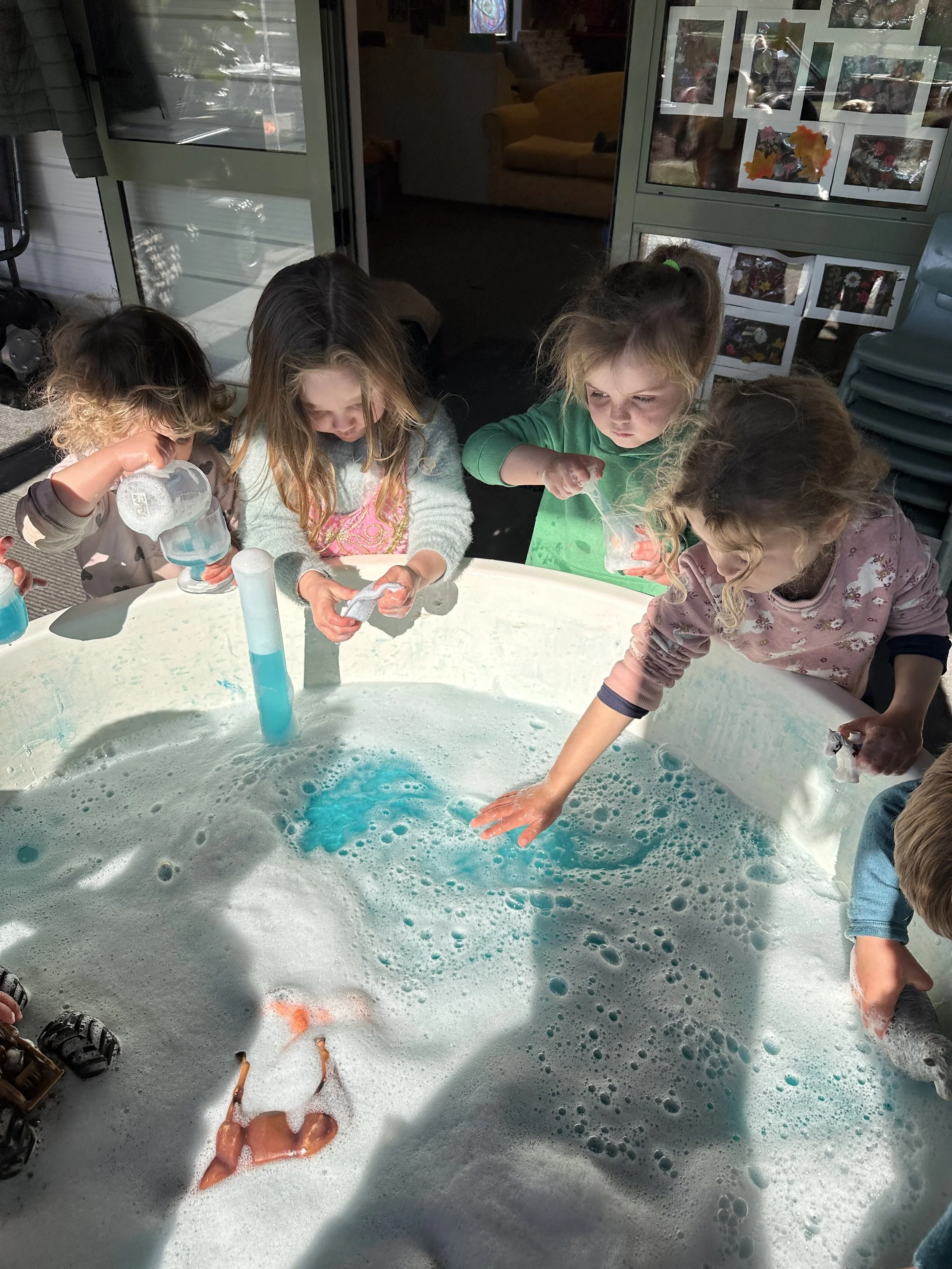Children playing in a foamy water table outdoors, engaging with colorful toys and bubbles.