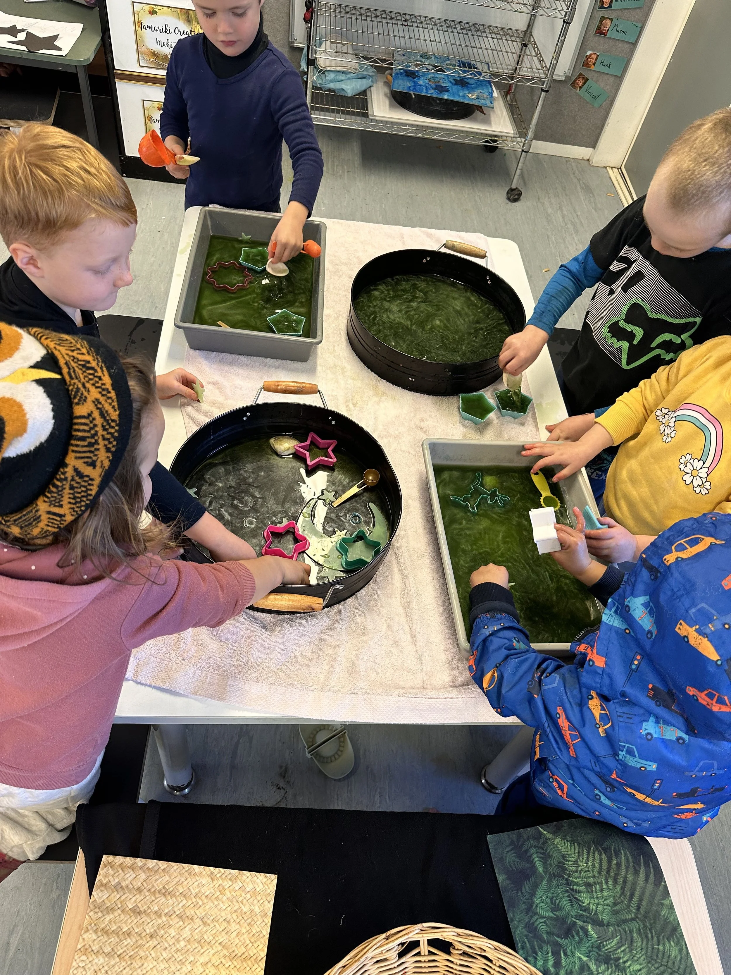 Children making and playing with colorful soap or slime in trays at a table.