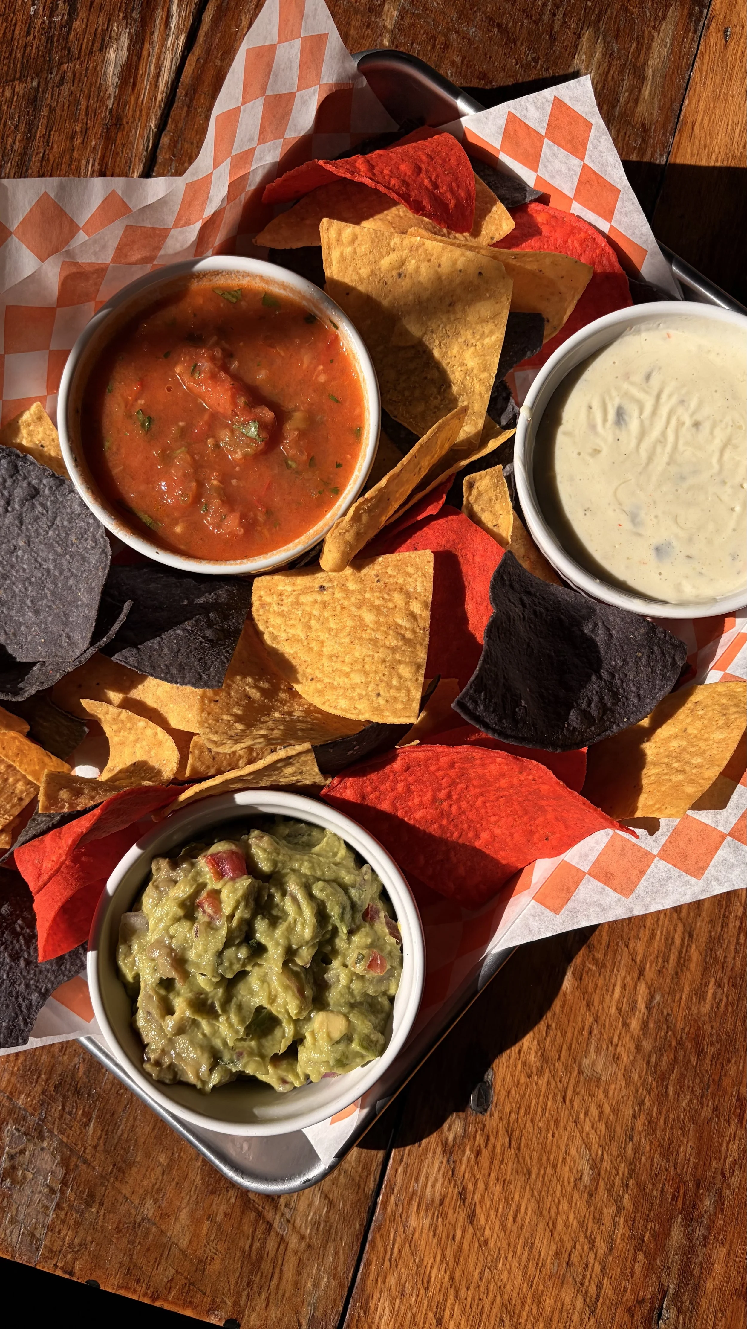 A tray with assorted nachos, salsa, guacamole, and sour cream on a wooden table.