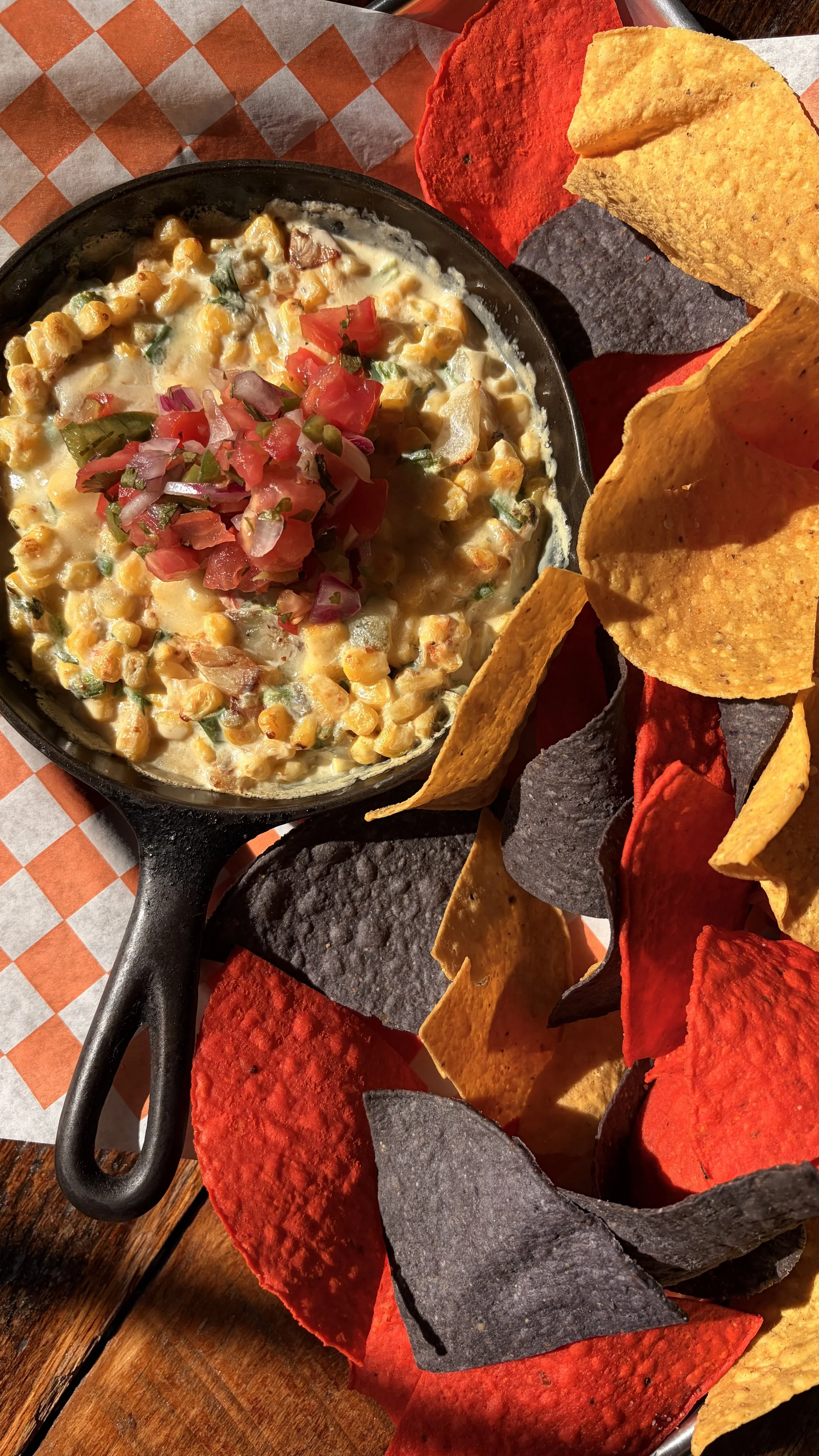 Bowl of creamy corn with roasted tomatoes and onions, served with multicolored tortilla chips.