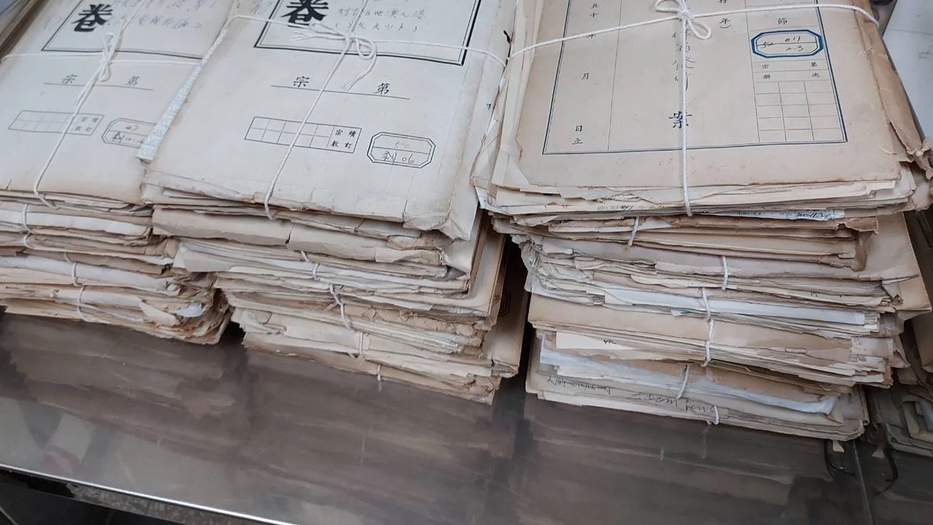 Stacks of old, weathered paper documents tied with string, stored on a metal surface.