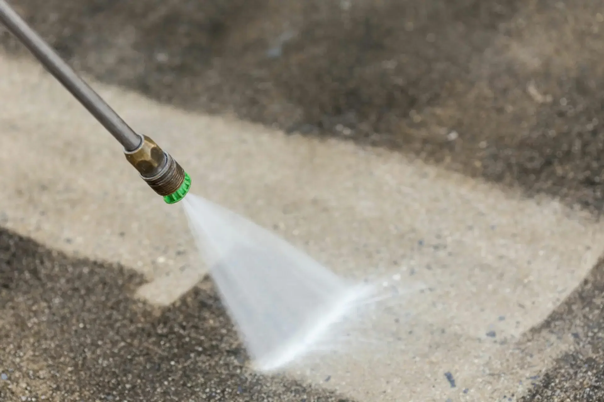 A pressure washer nozzle spraying water onto a concrete surface.