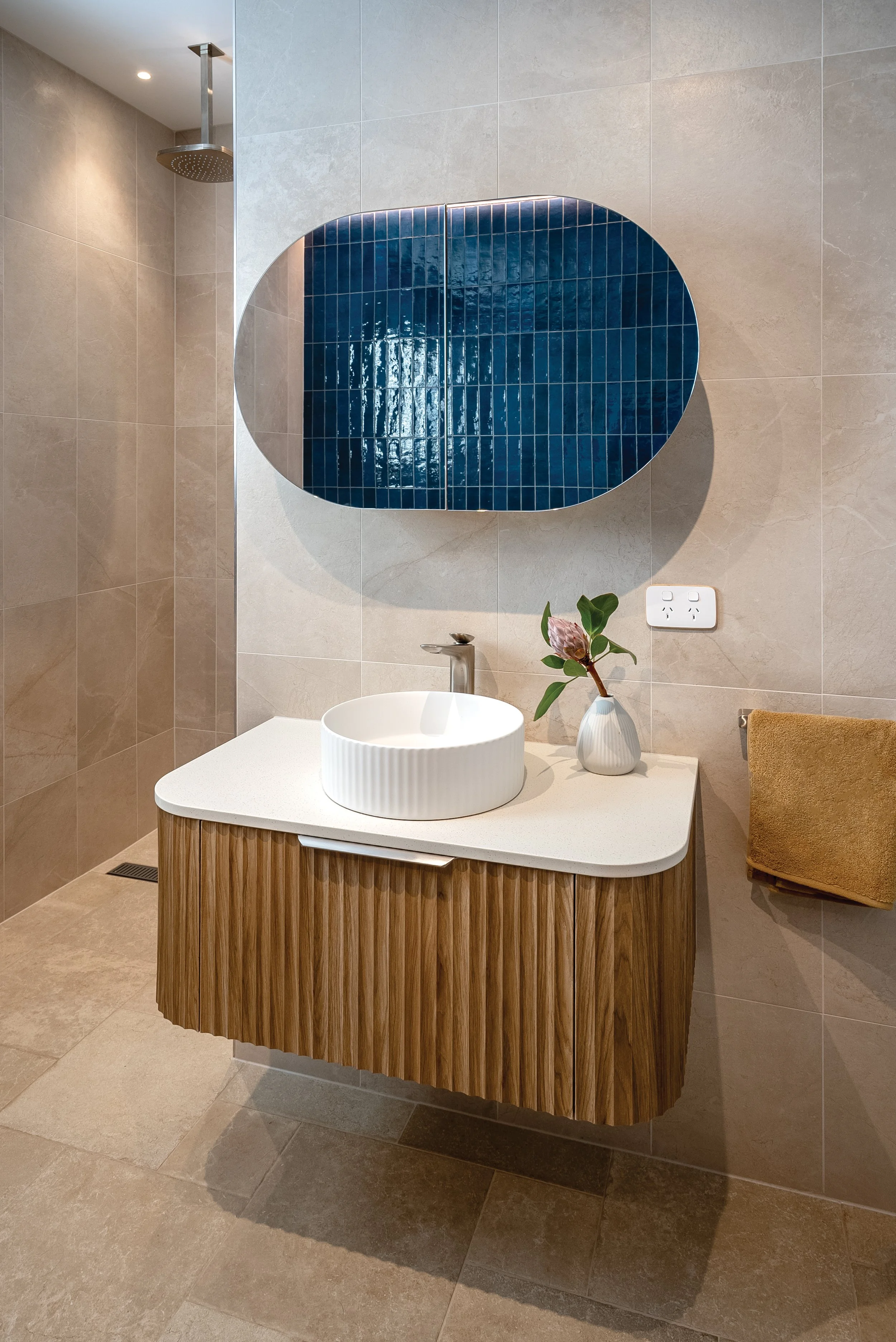 Modern bathroom with a floating vanity, vessel sink, small vase with a plant, a mirror, and a towel rack.