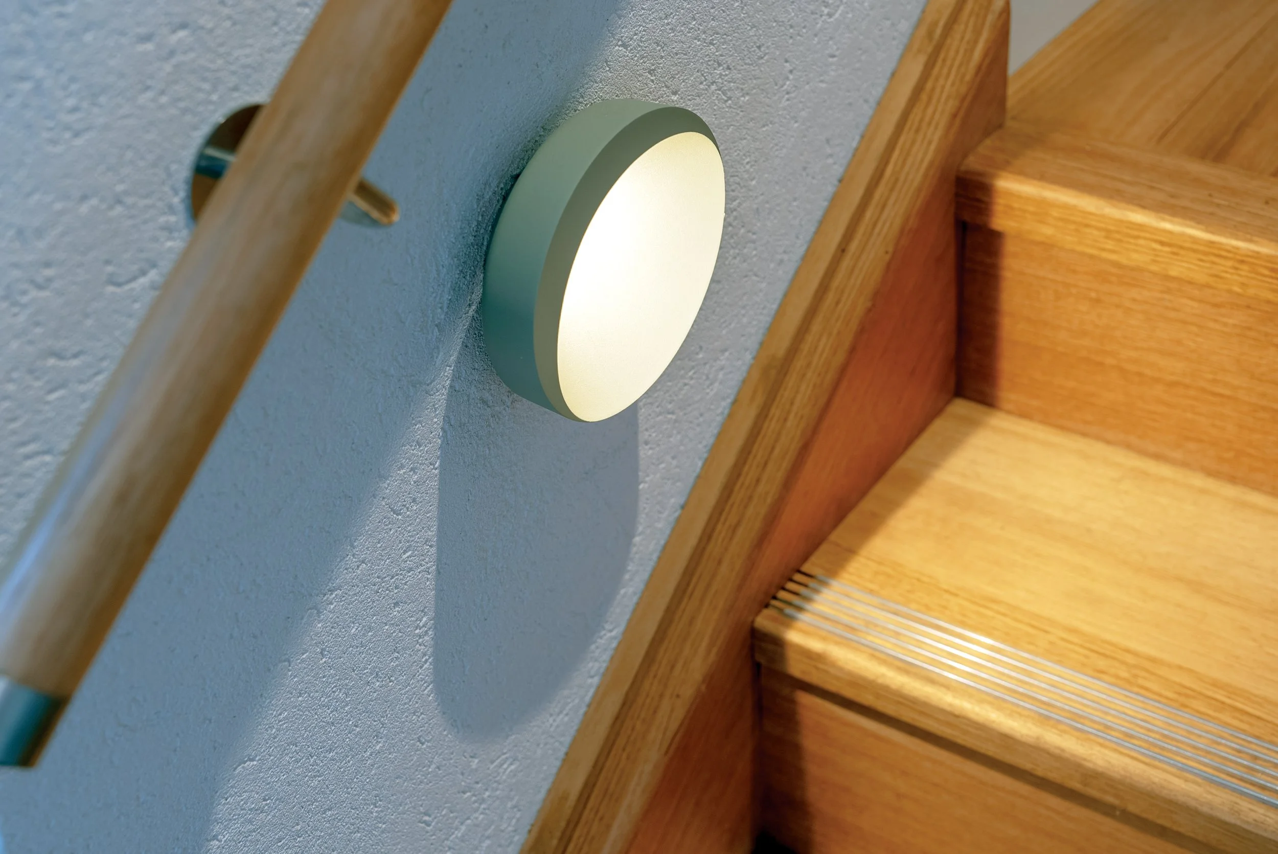 Close-up of a modern, crescent moon sconce light fixture emitting a soft yellow glow, next to timber staircase..