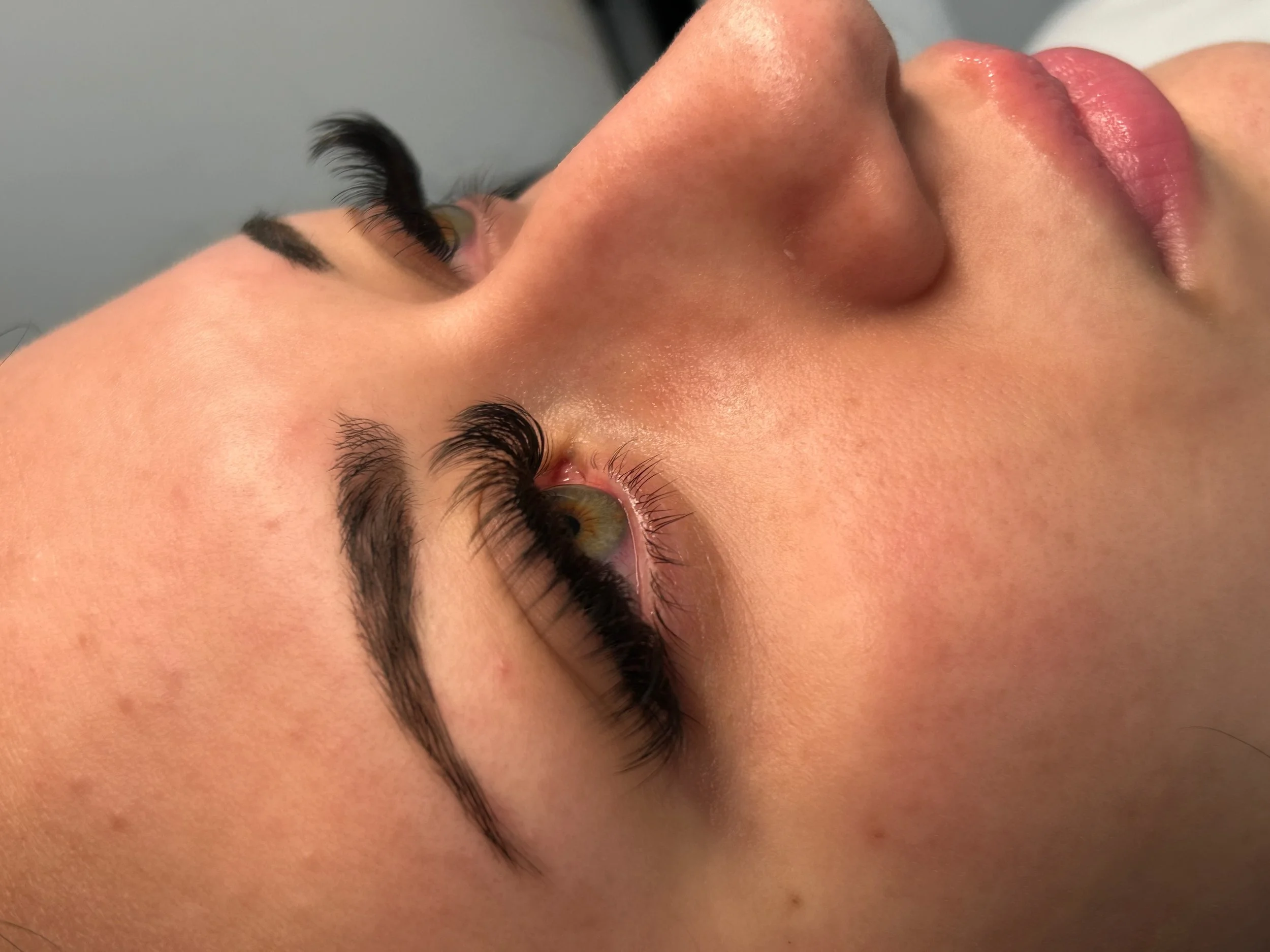 Close-up of a woman lying down with focus on her face, showing her eyes, nose, and lips. She has long, curled eyelashes and natural makeup.