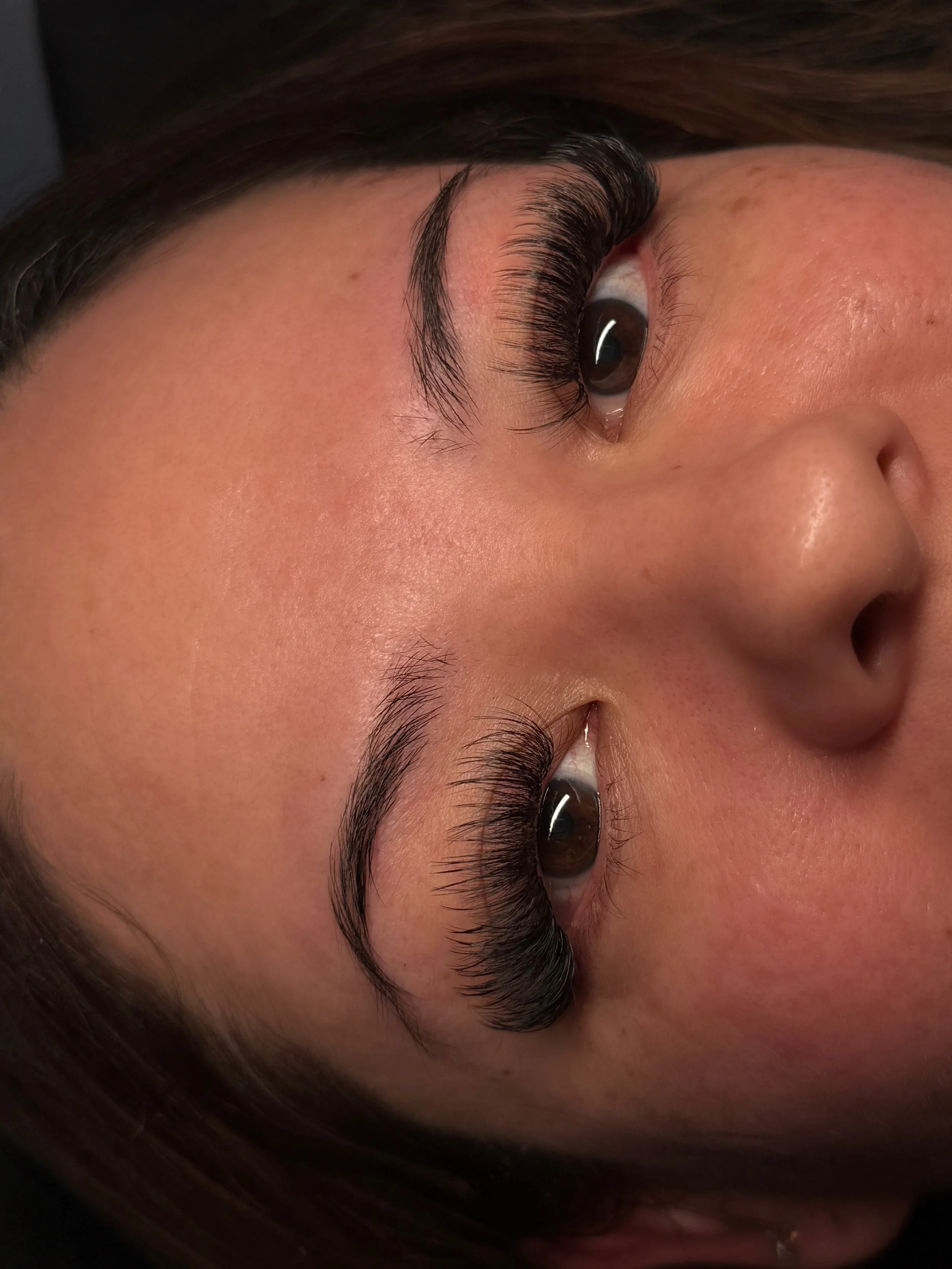 Close-up of a woman lying down with long, curled eyelashes, smooth skin, and dark eyebrows.