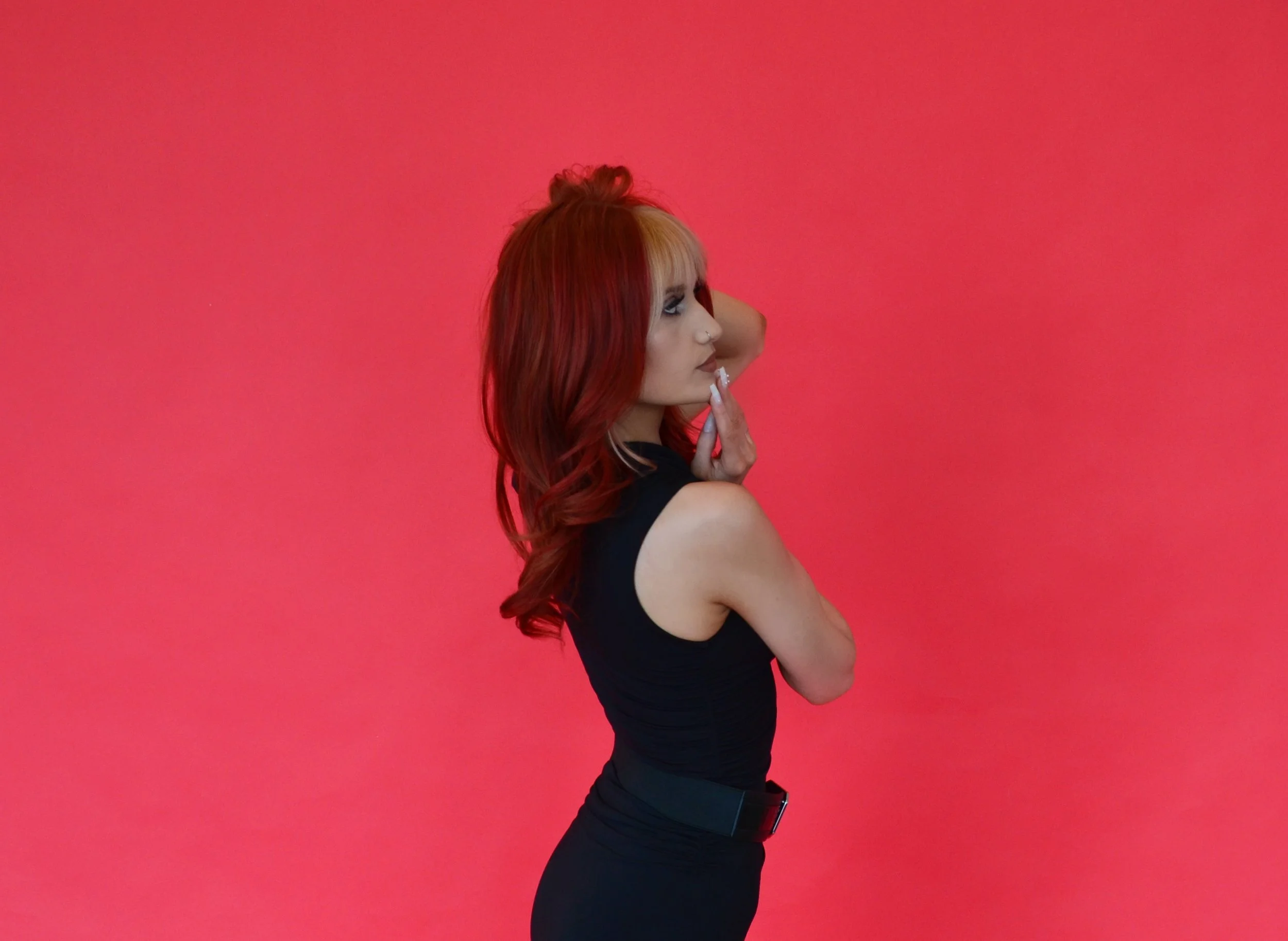 A woman with red hair and a side profile pose against a pink background.