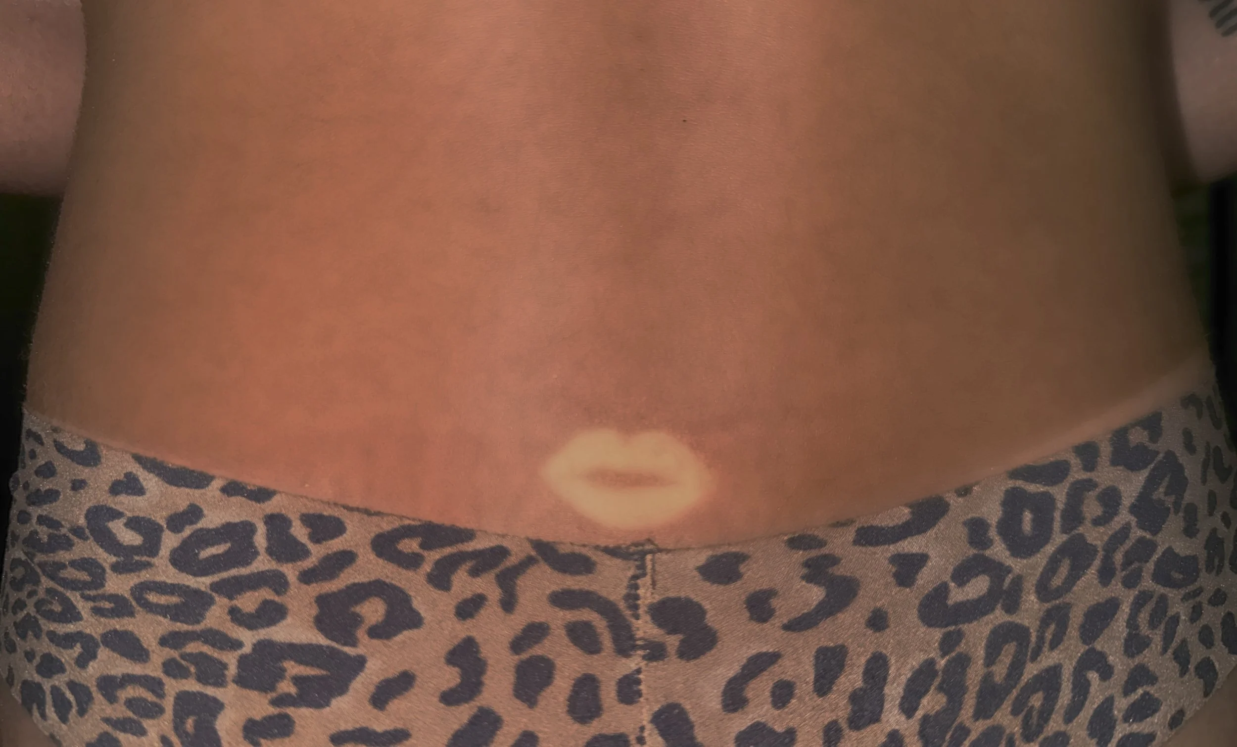 Close-up of a person's lower abdomen with a tattoo of lips just above the patterned waistband of leopard print underwear.
