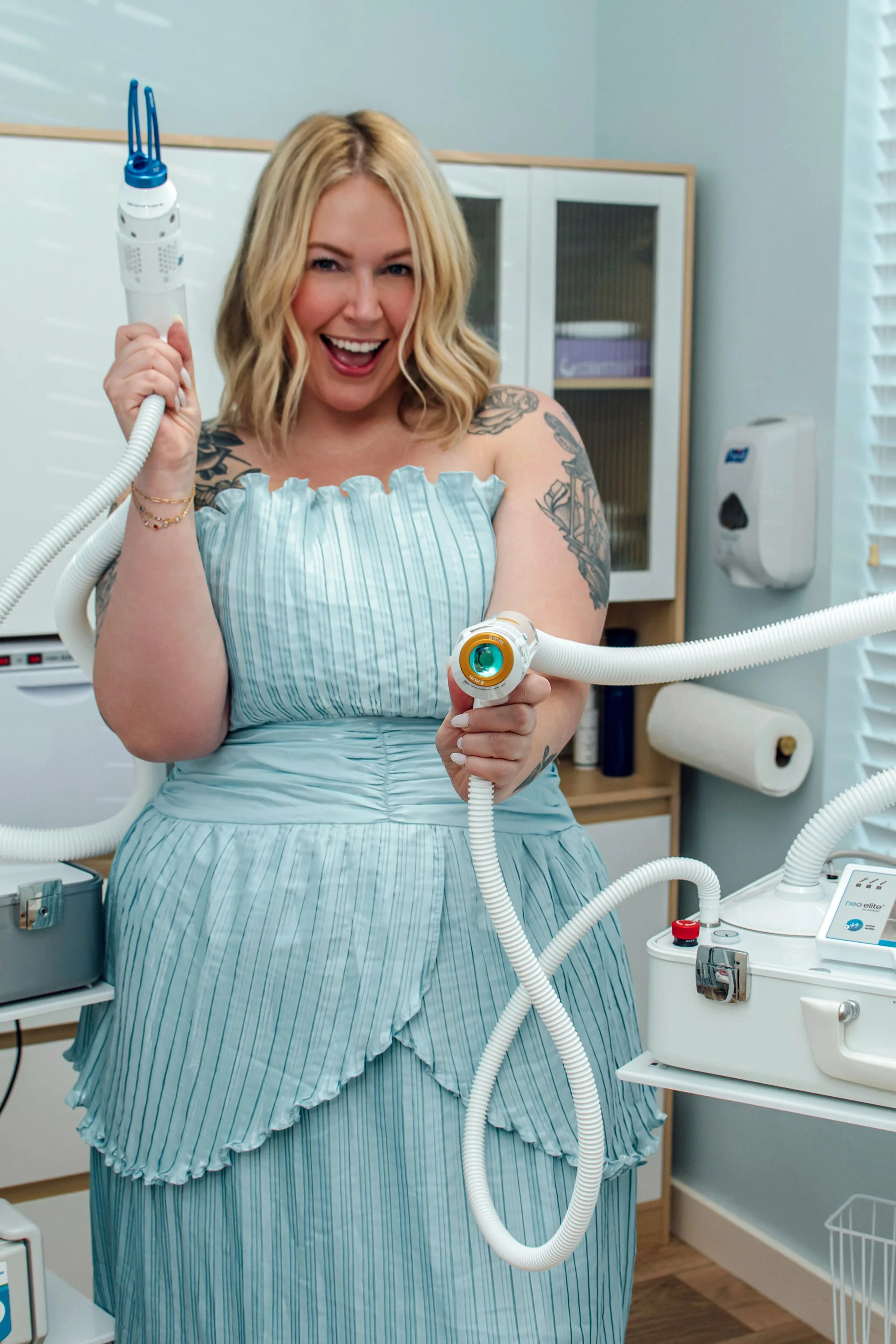 Woman in a hospital gown holding a medical device, surrounded by medical equipment in a clinical setting.