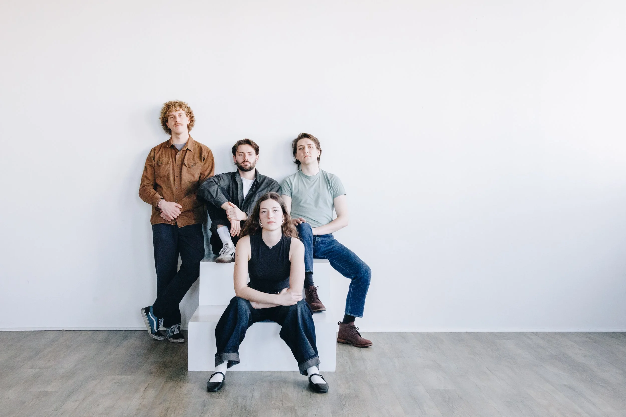 Four young adults posing against a plain white wall in a minimalistic setting.