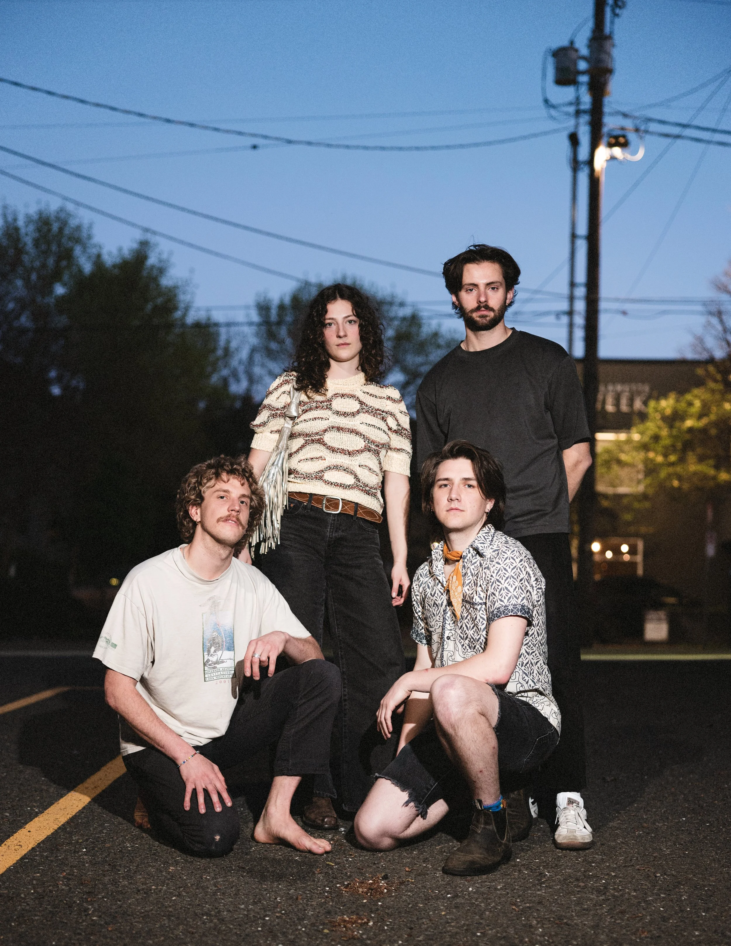 Group of five young adults posing on a street at dusk with power lines and trees in the background.