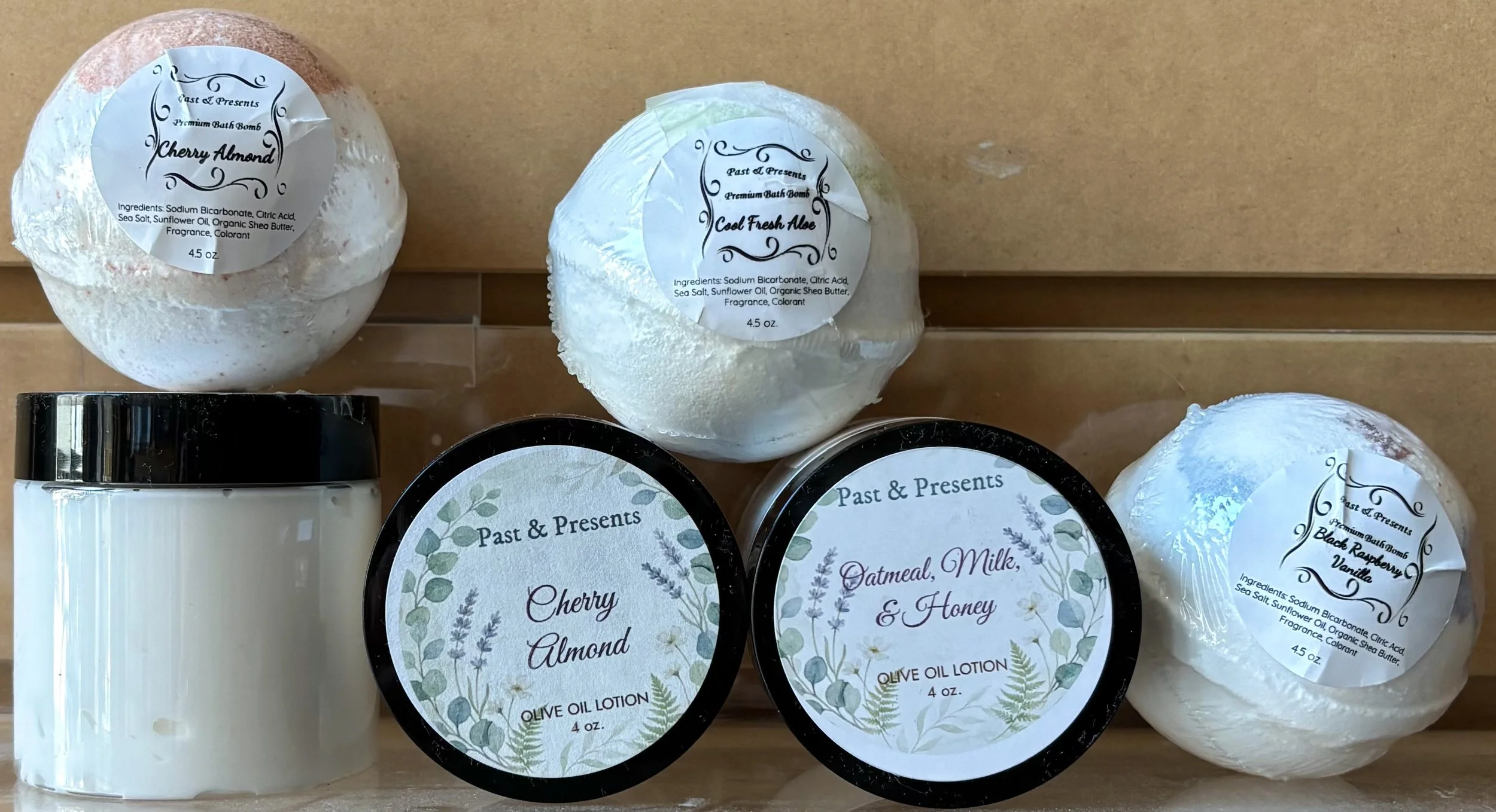 Assorted bath products including bath bombs and lotion from the brand Past & Presents, with scent labels such as Cherry Almond, Cool Fresh Aloe, Black Raspberry & Vanilla.
