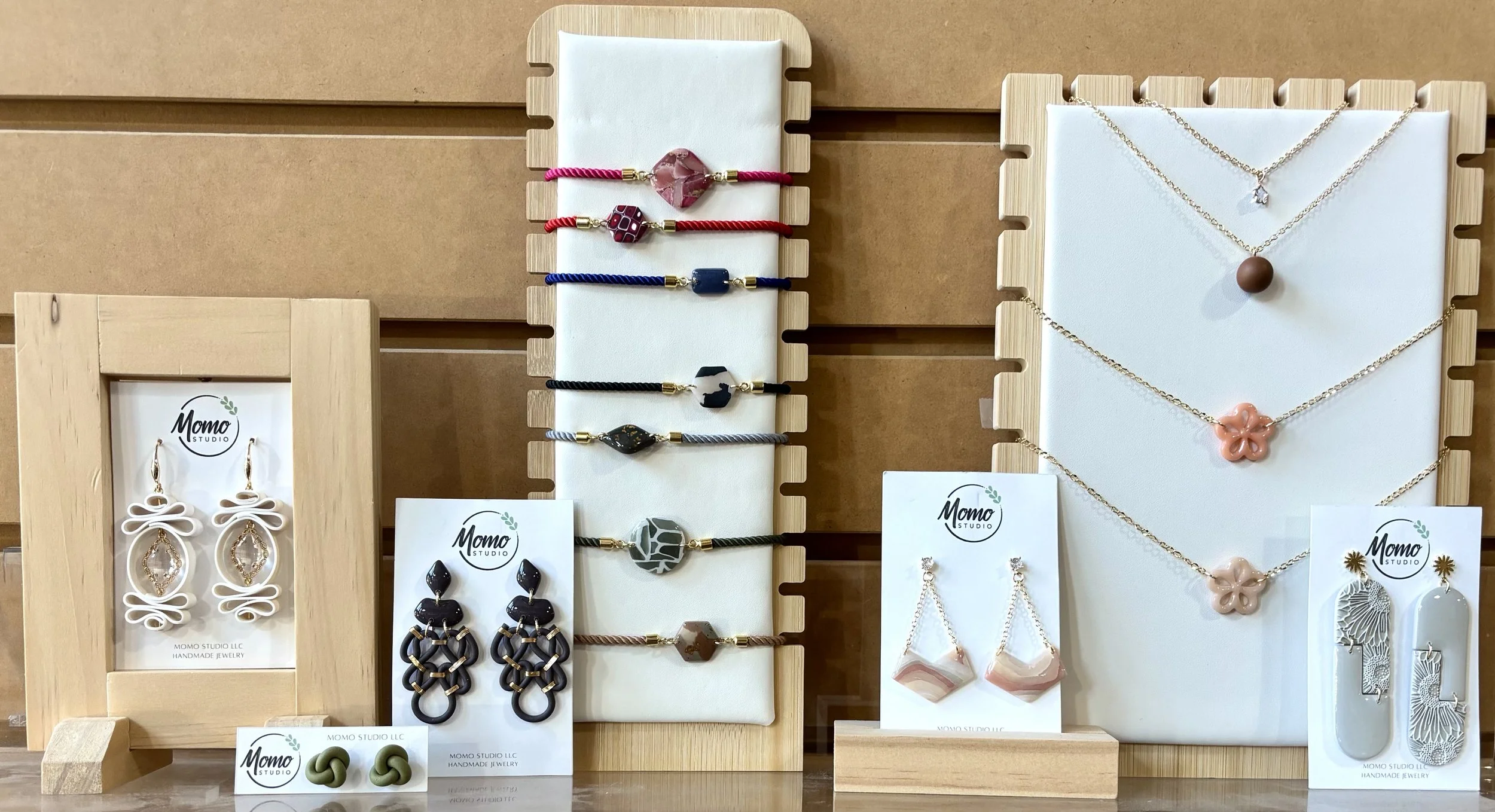 Display of handmade jewelry including bracelets, necklaces, and earrings on wooden and white stands.