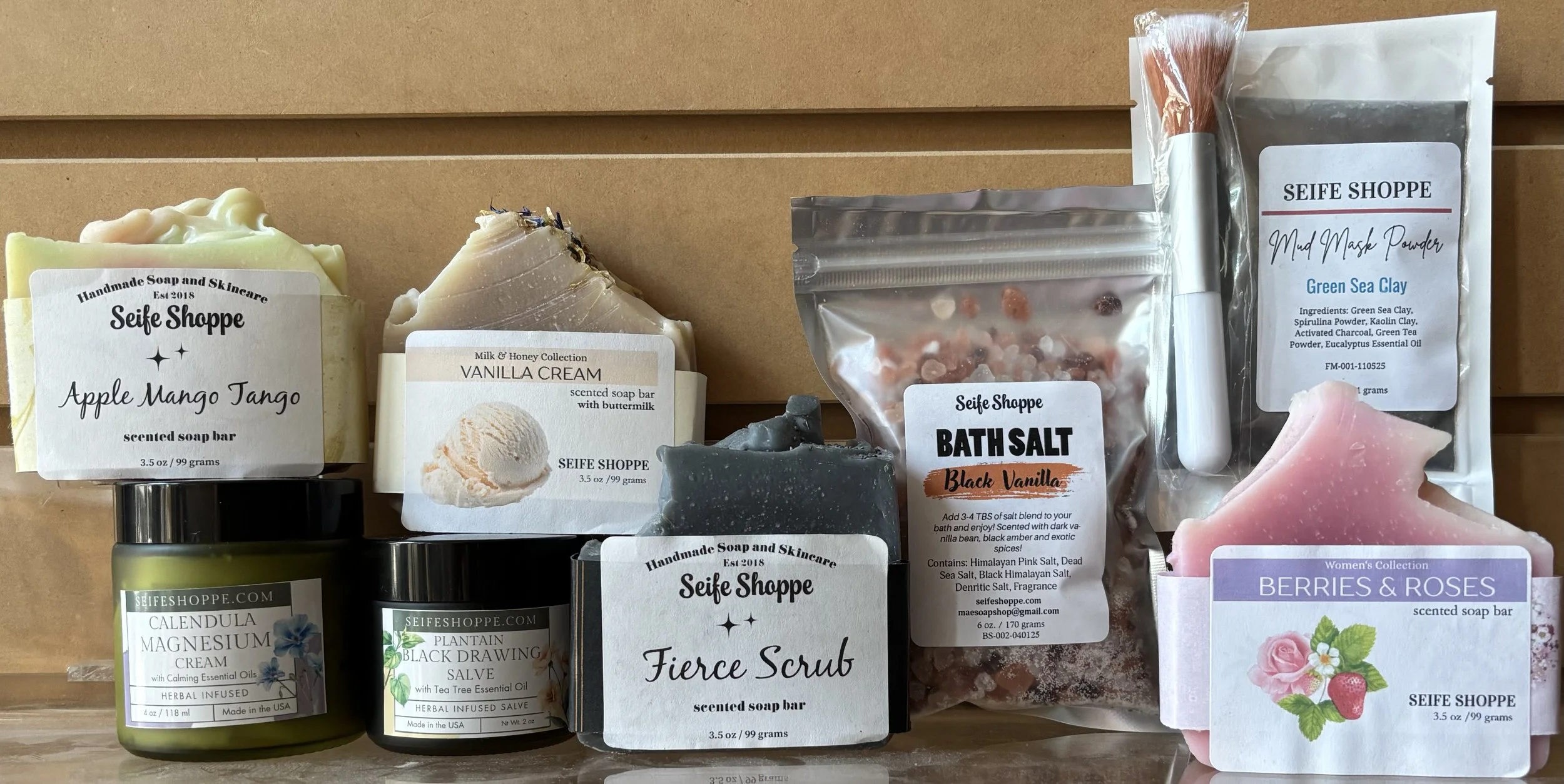 A display of handmade soap bars and products, including apple mango tango scented soap, vanilla cream soap, bath salts, and other skincare items.