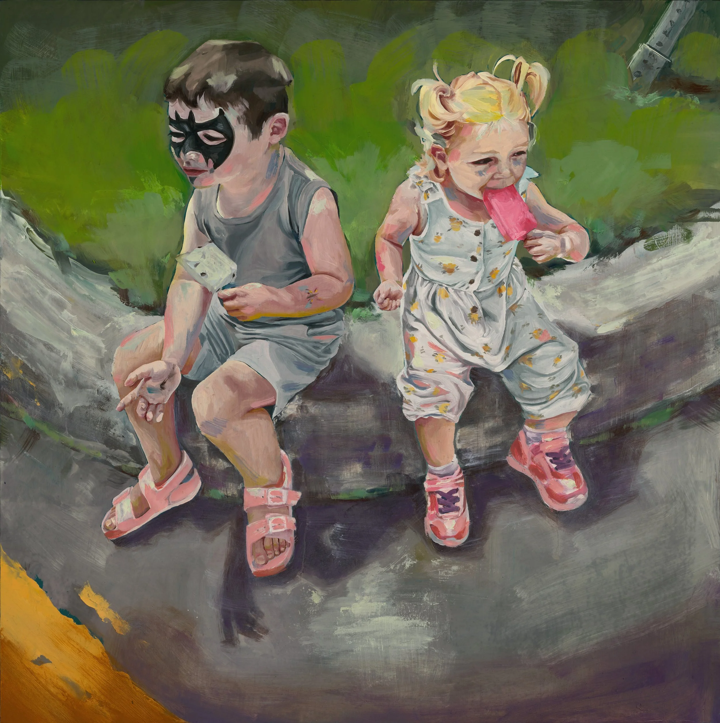 Two young children sit on a large fallen tree trunk outdoors. The boy on the left wears a dark mask, gray sleeveless shirt, shorts, and pink sandals, holding a small object. The girl on the right wears a floral dress, pink and purple shoes, and is licking a pink popsicle.