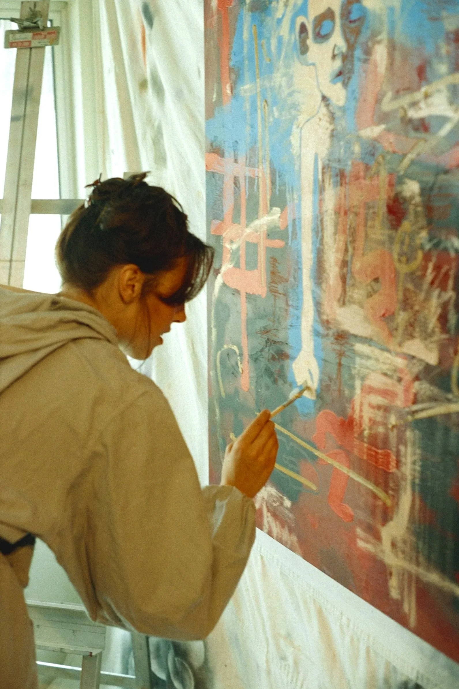 A woman is painting on a large colorful abstract canvas with a paintbrush.