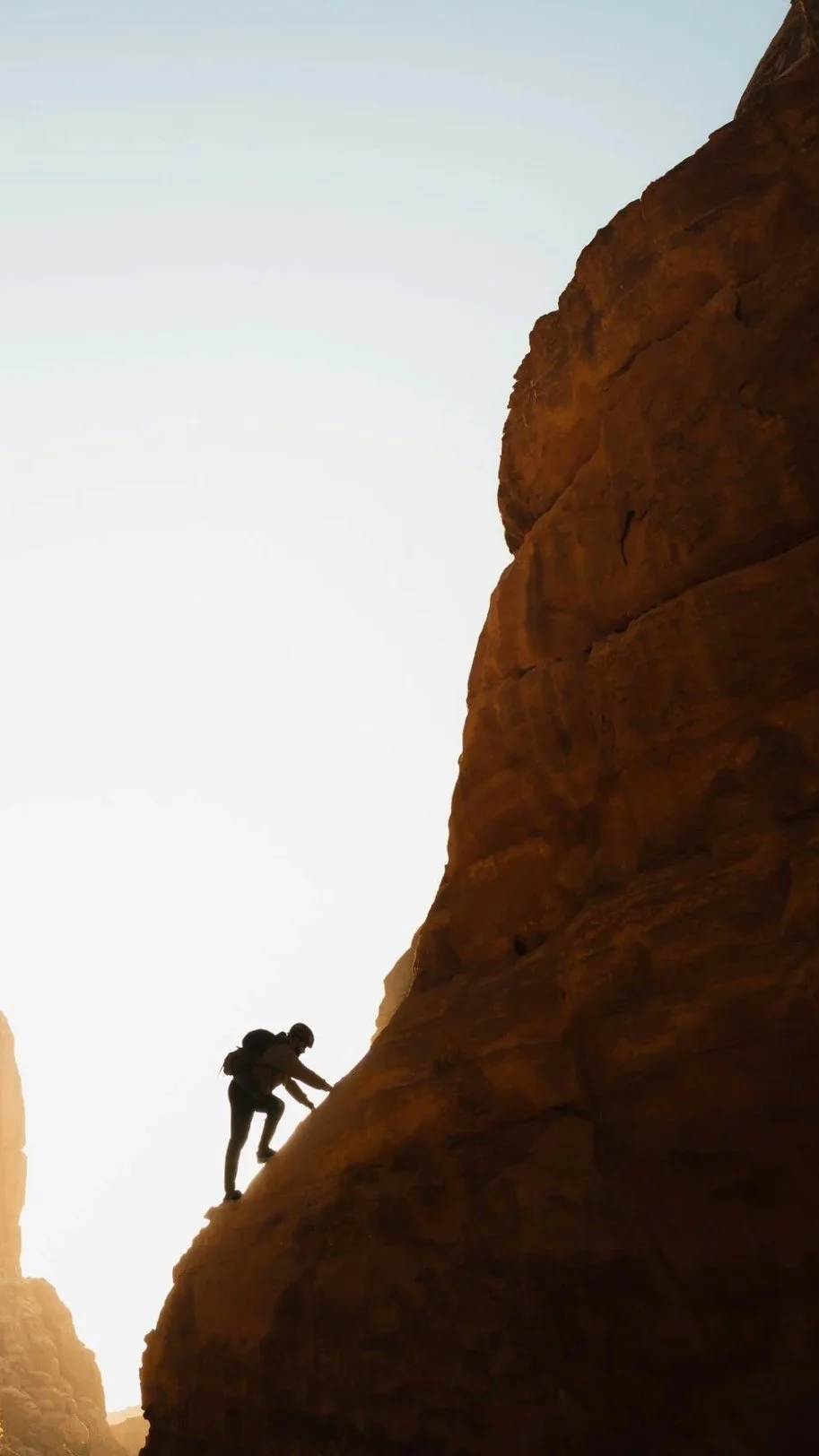 A person climbing a steep rock formation in a canyon during sunrise or sunset.