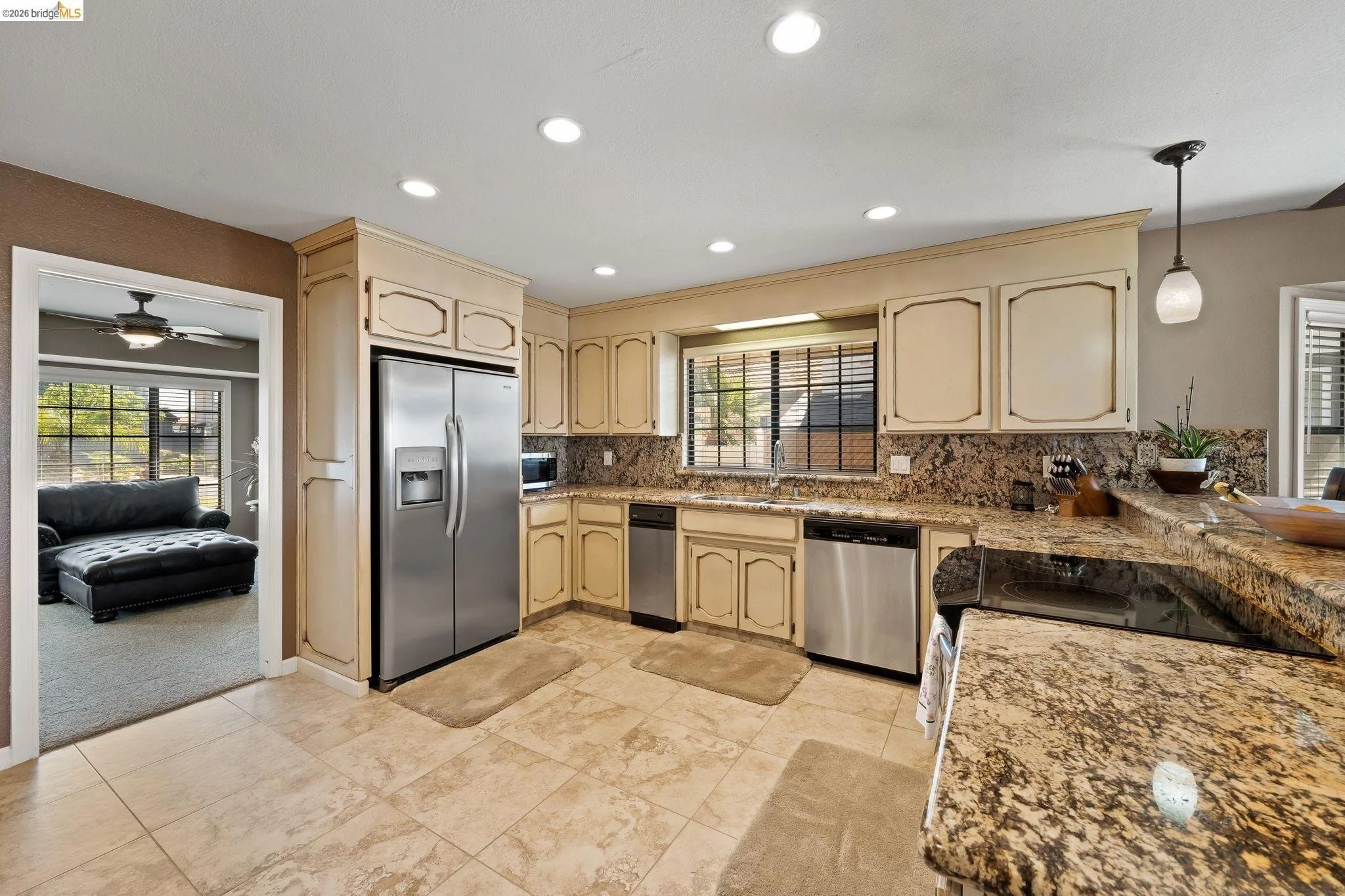 Kitchen with beige cabinetry, granite countertops, stainless steel refrigerator, dishwasher, and oven, beige tile flooring, window above sink, and small pendant light